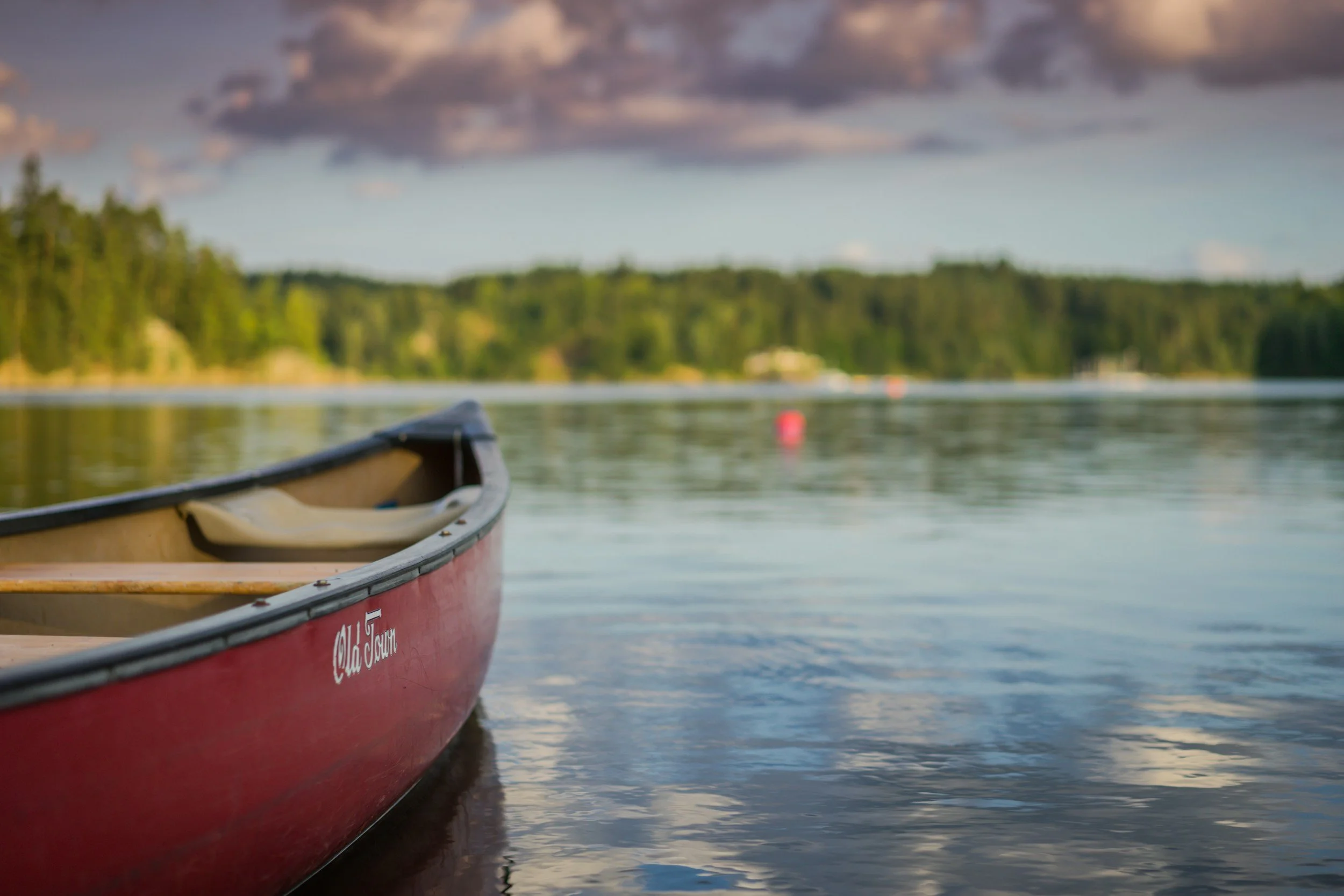 Red canoe on a calm lake with forested shoreline in the background.
