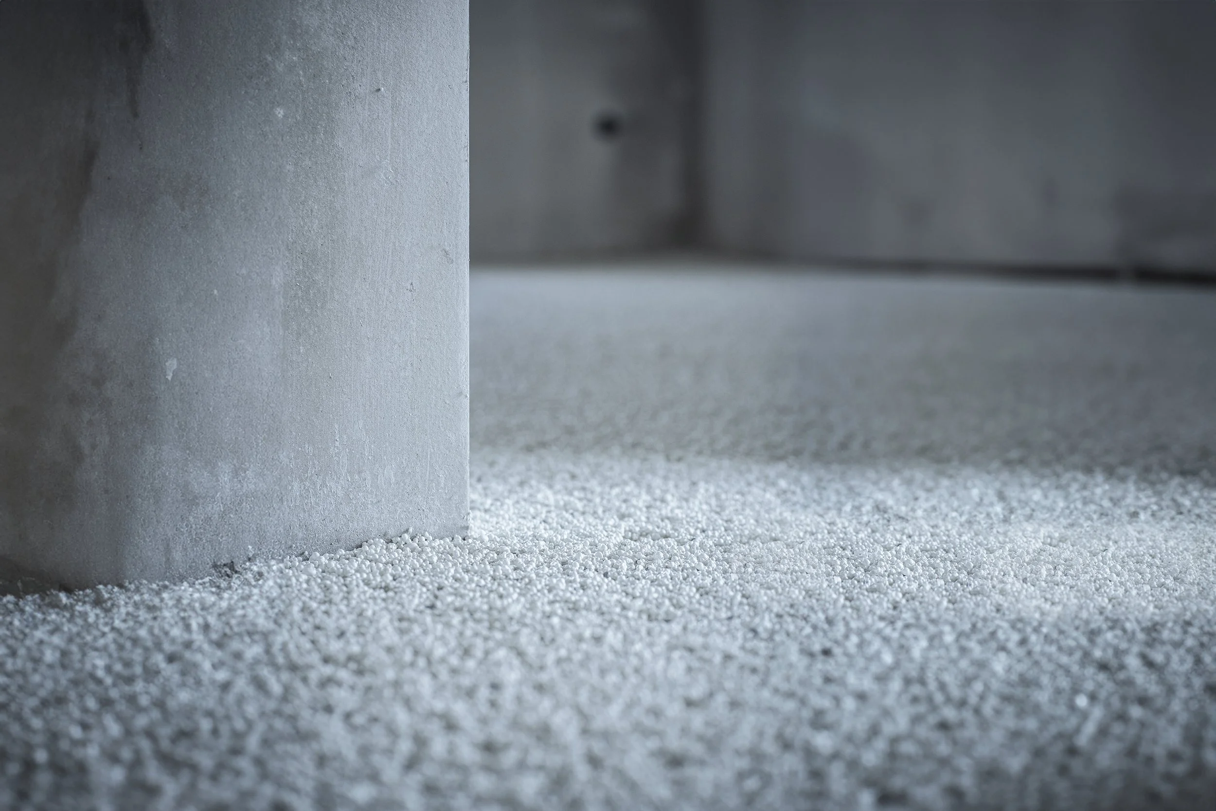 Close-up van een betonnen pilaar en een vloer bedekt met kleine witte korrels Thermowhite vloerisolatie.
