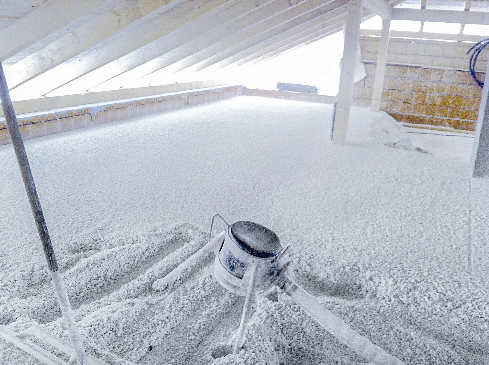 Zolder met een afgekleurde vloerbedekking die bedekt is met Thermowhite isolatiemateriaal. Er staat een rode beschermingsdrager en een verfbeker, geen mensen zichtbaar.