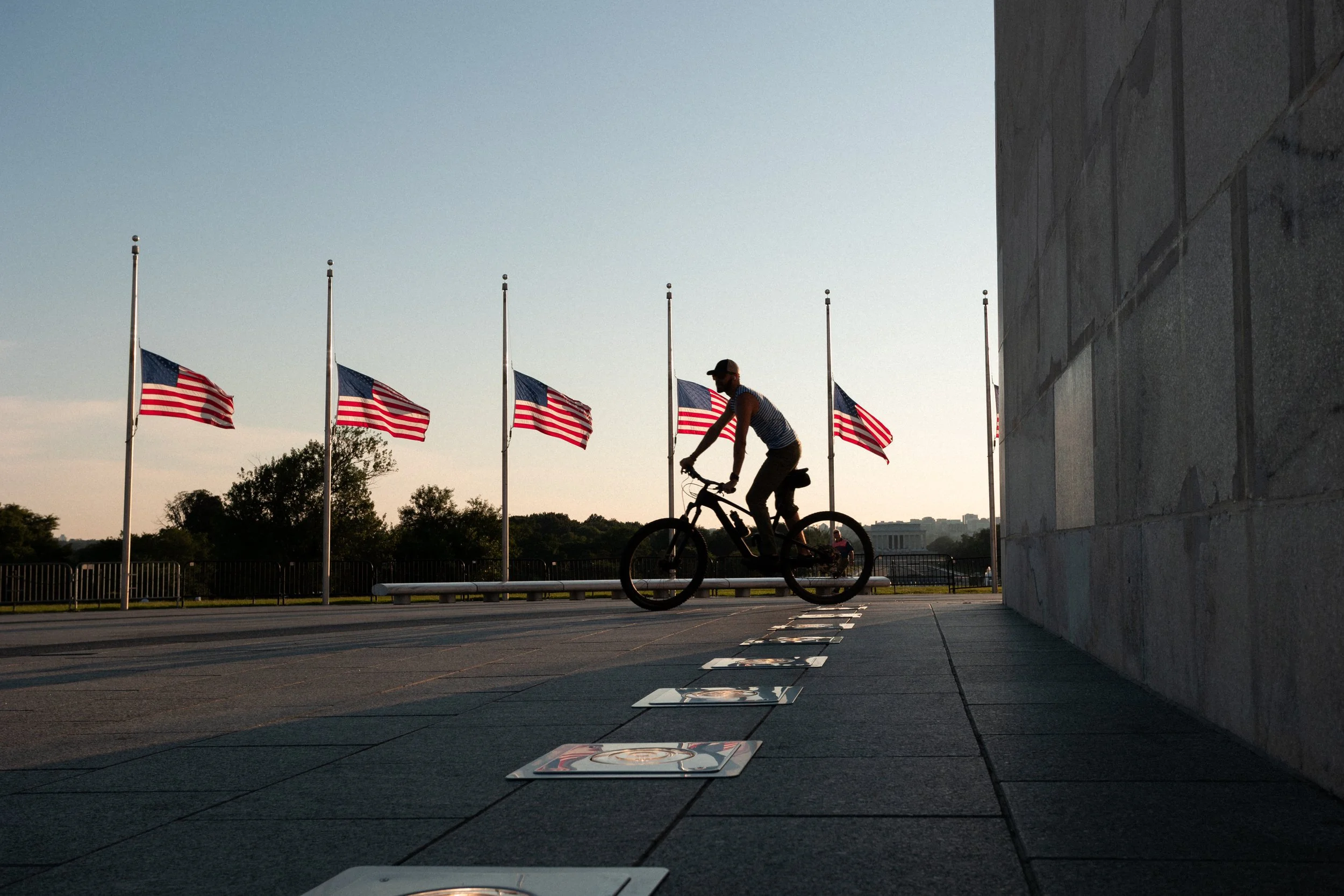 A person riding a bicycle past rows of American flags during sunset near the Lincoln Memorial.