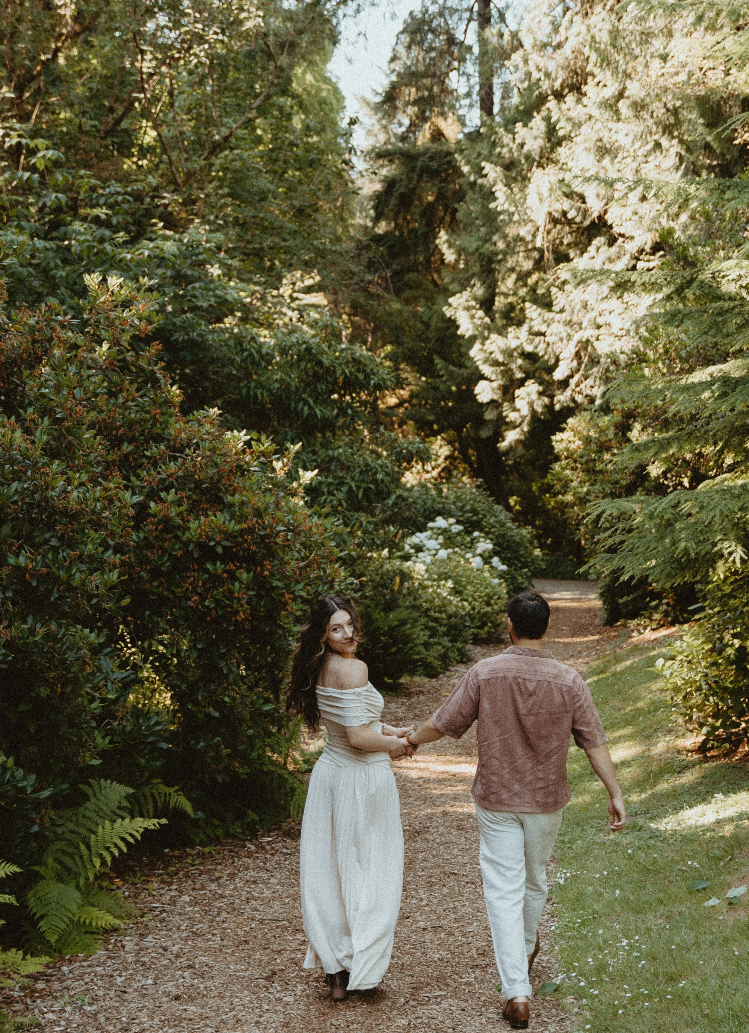 Woman looking back while walking with partner through greenery + romantic movement + Seattle engagement session + PNW photography