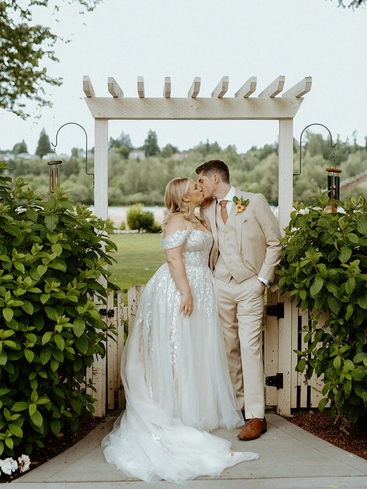 Bride and groom kissing under white garden arbor during outdoor wedding at Kelley Farm