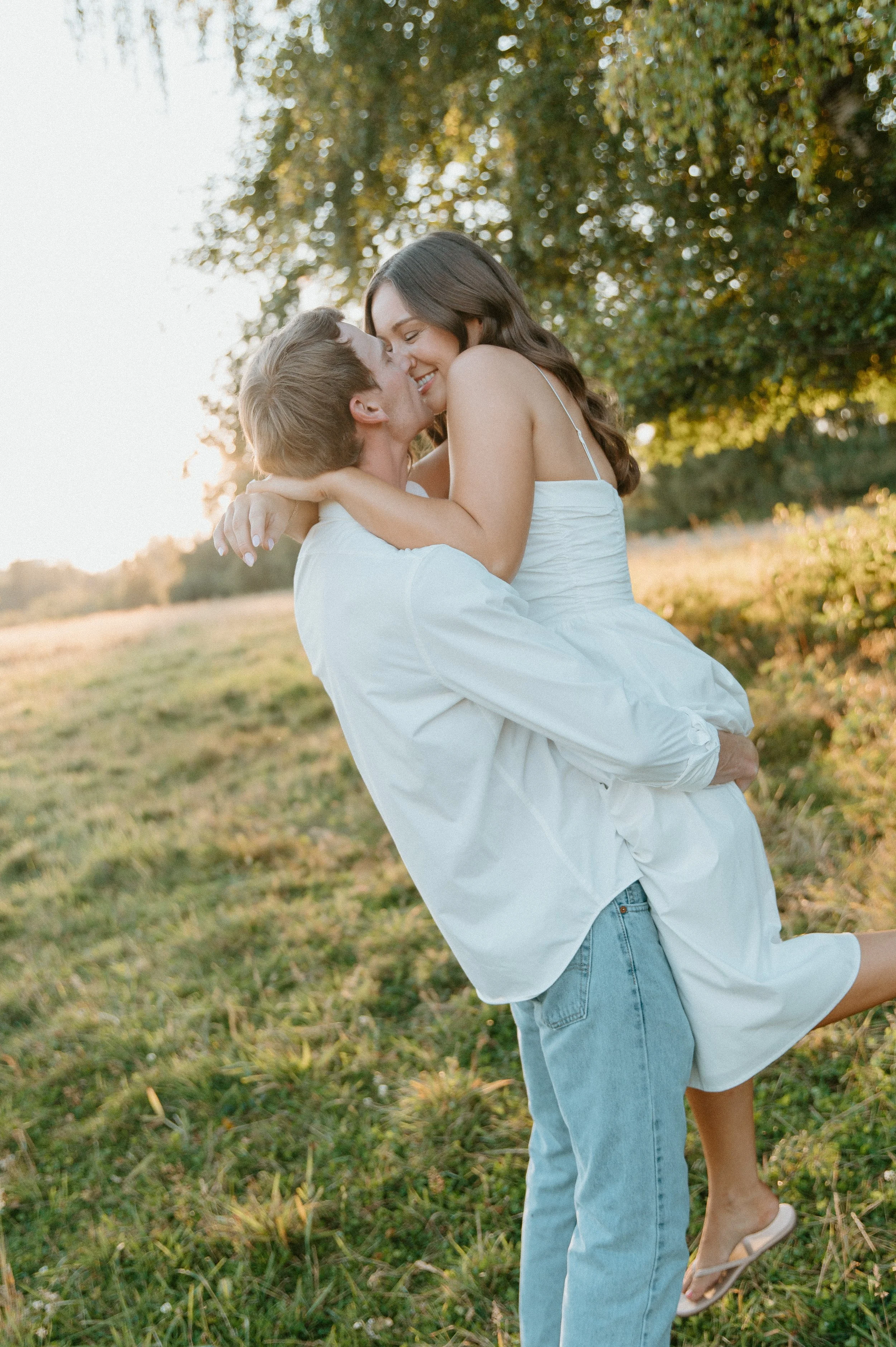 Engaged couple laughing and embracing as he lifts her in a sunlit field during their North Bend engagement session