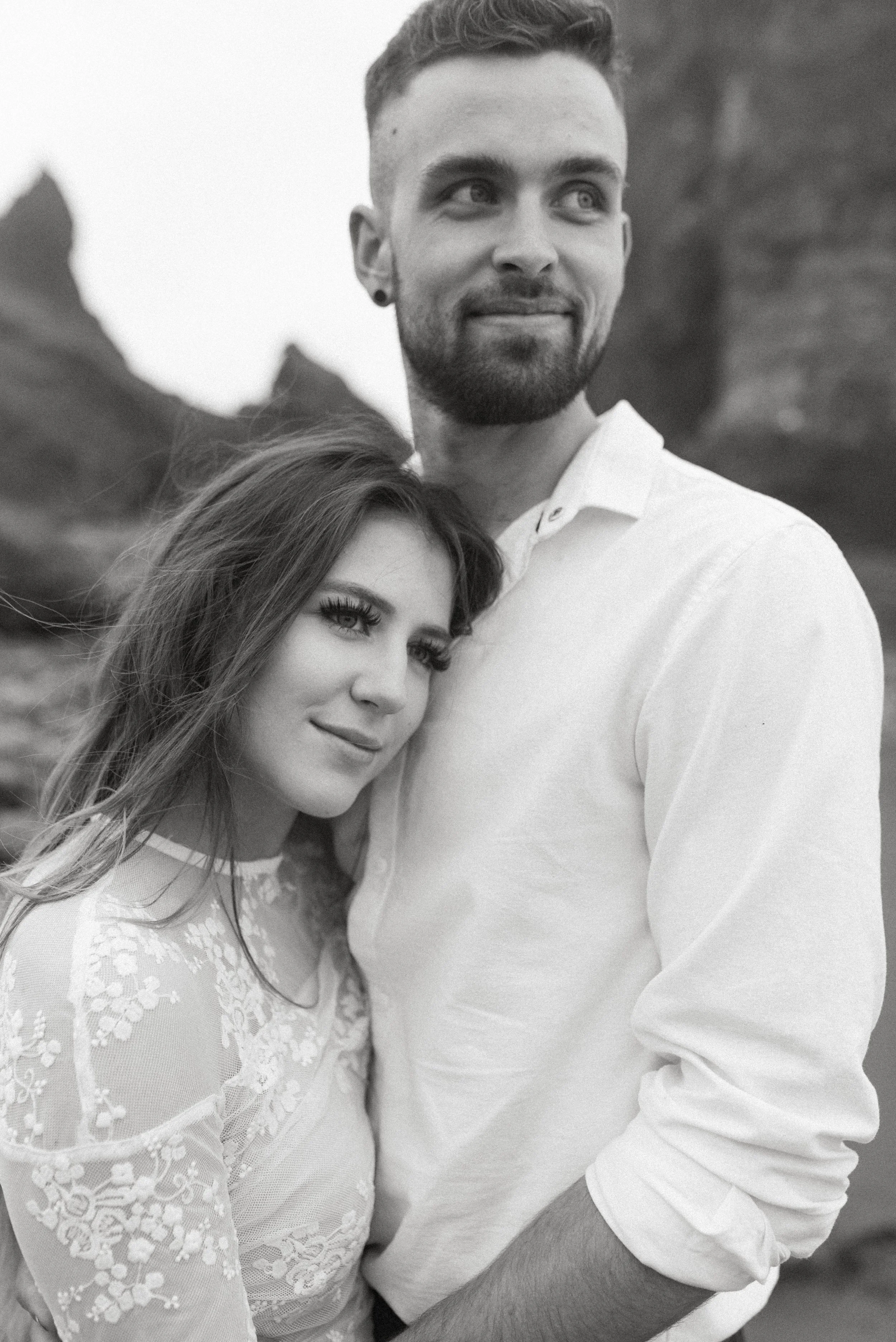 Black and white portrait of bride and groom embracing on Cannon Beach with dramatic coastal rock formations in the background