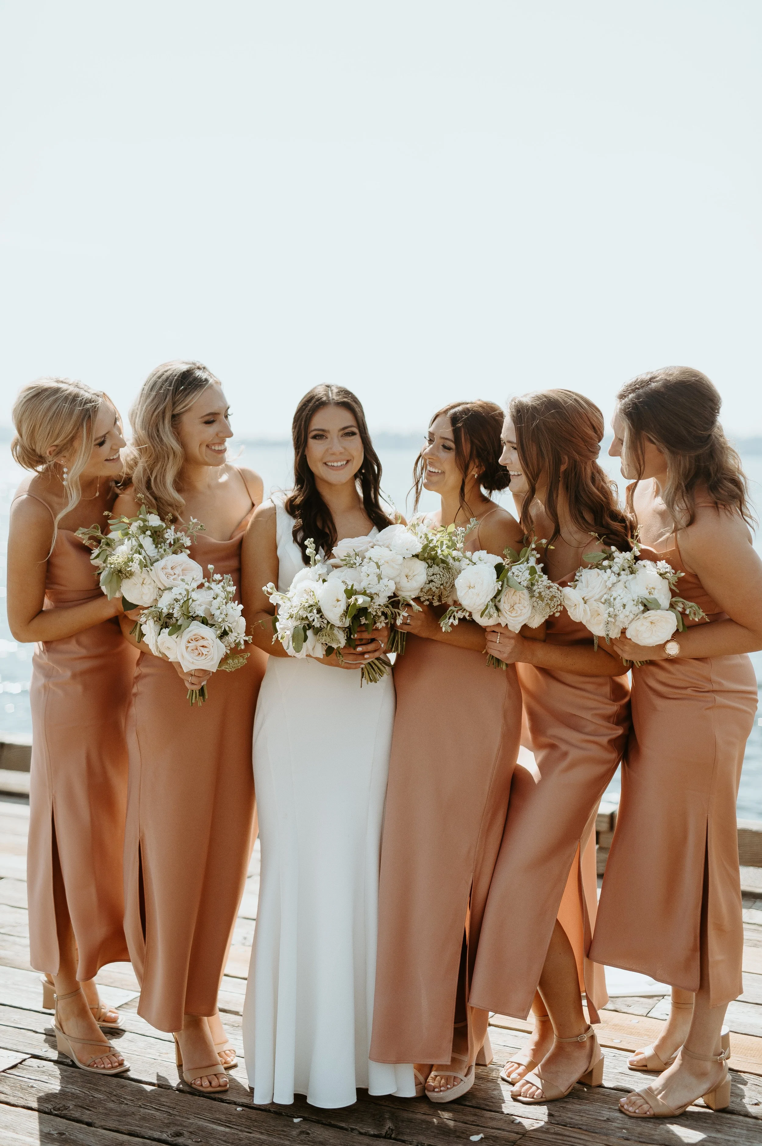 Bride with bridesmaids in neutral-toned dresses holding white bouquets + bridal party portraits + Woodinville wedding + waterfront wedding