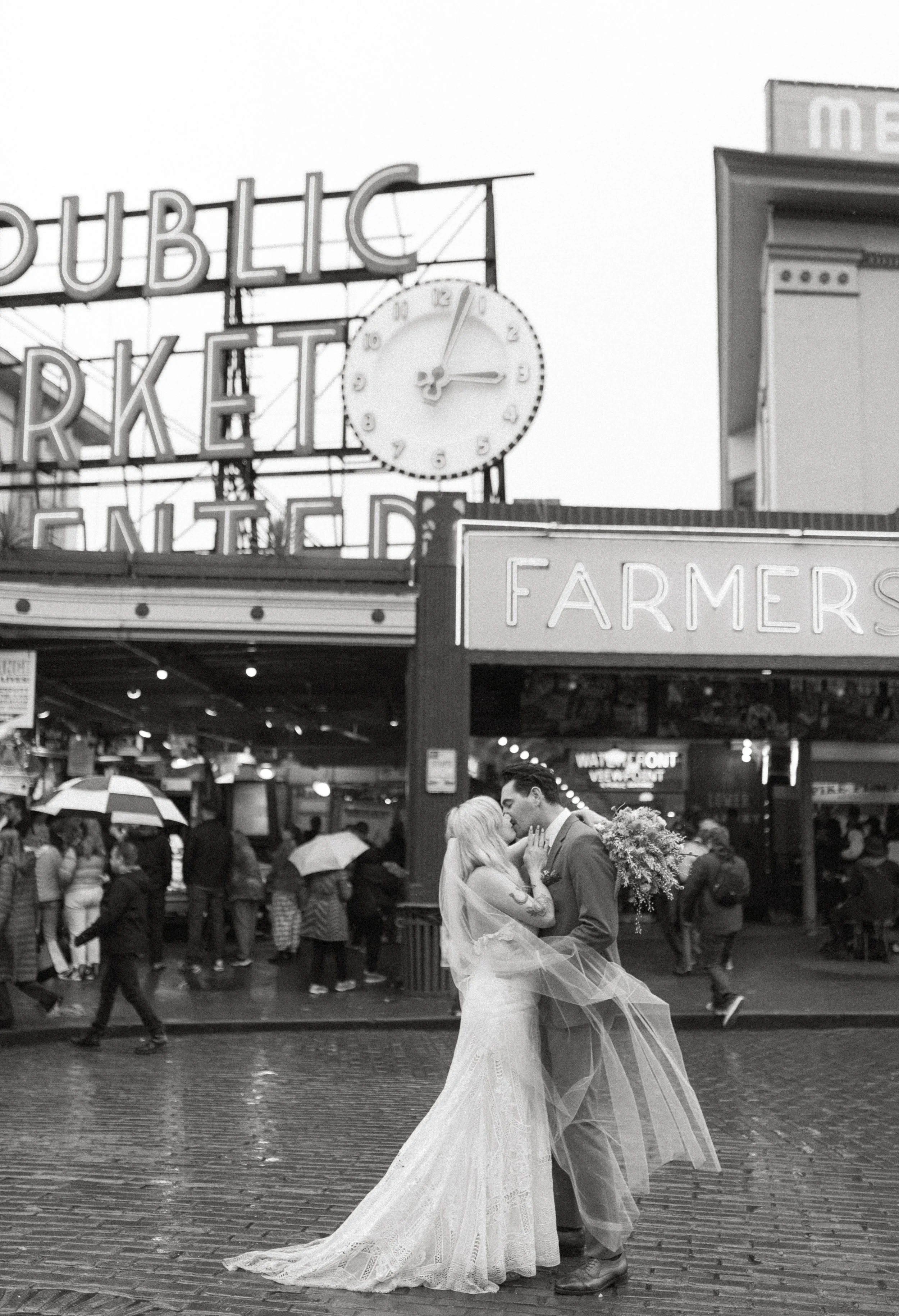 Bride and groom embracing in front of Pike Place Market sign during a downtown Seattle elopement