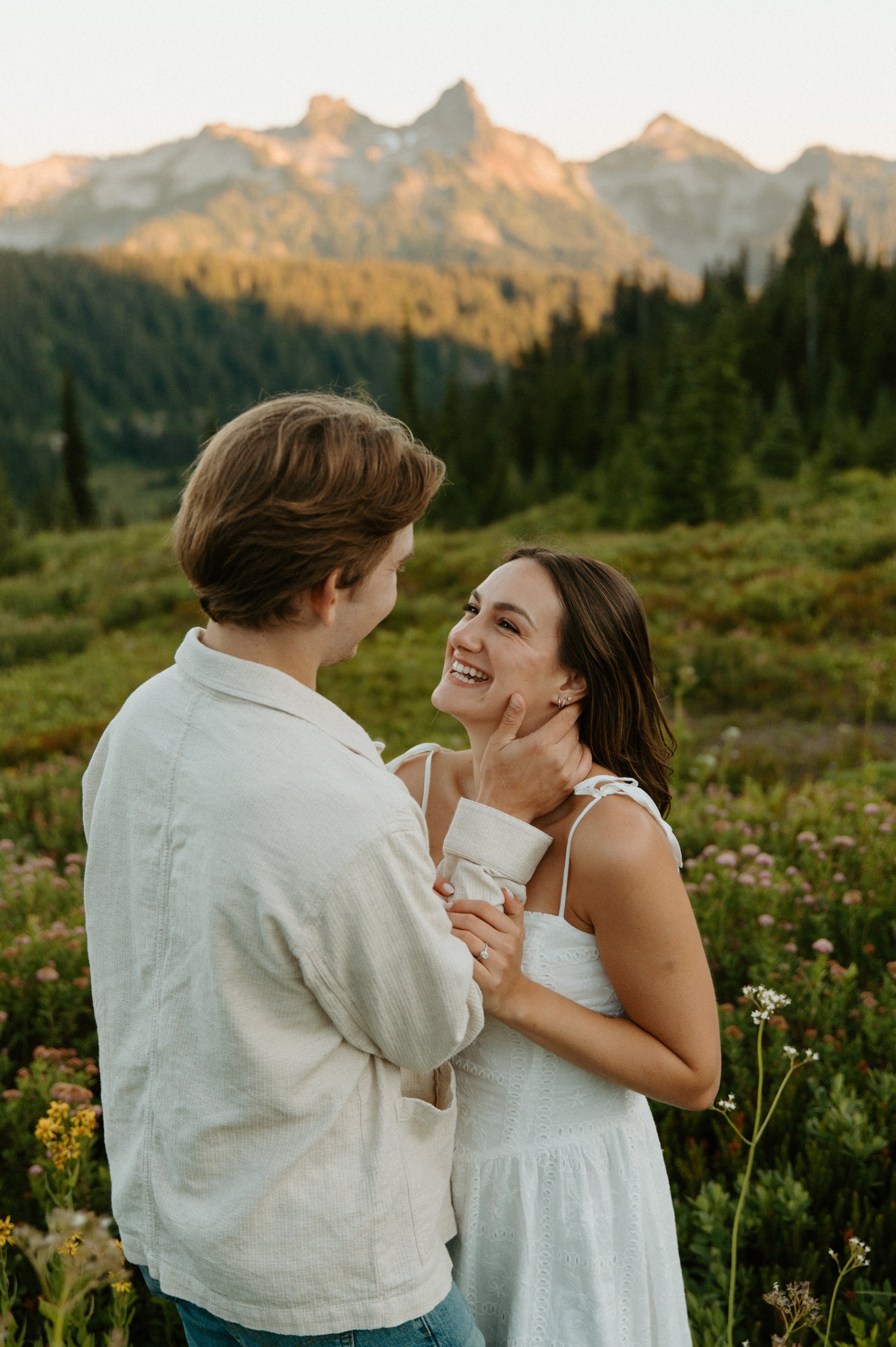 Bride-to-be smiling up at her fiancé while relaxing together in a mountain meadow.