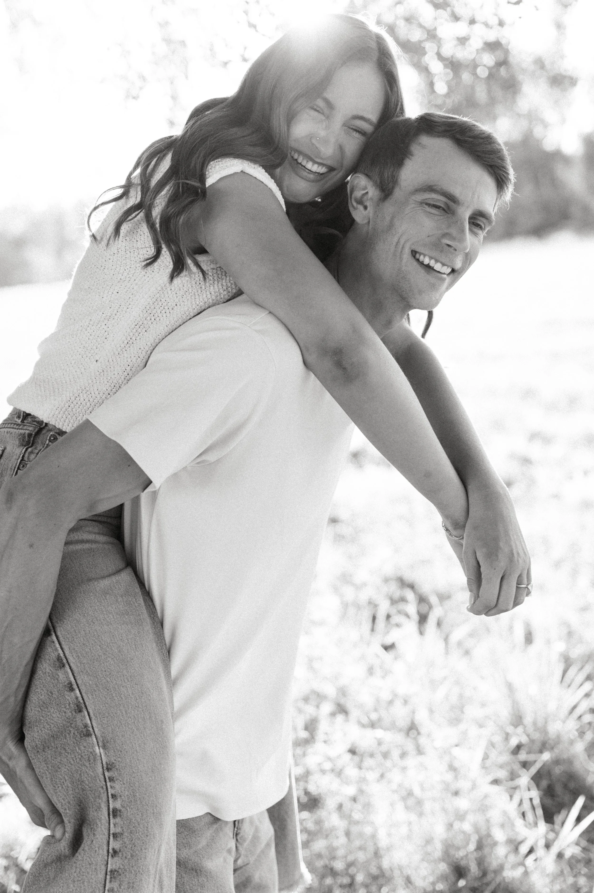 Black-and-white photo of an engaged couple laughing during a playful piggyback ride at their North Bend engagement session
