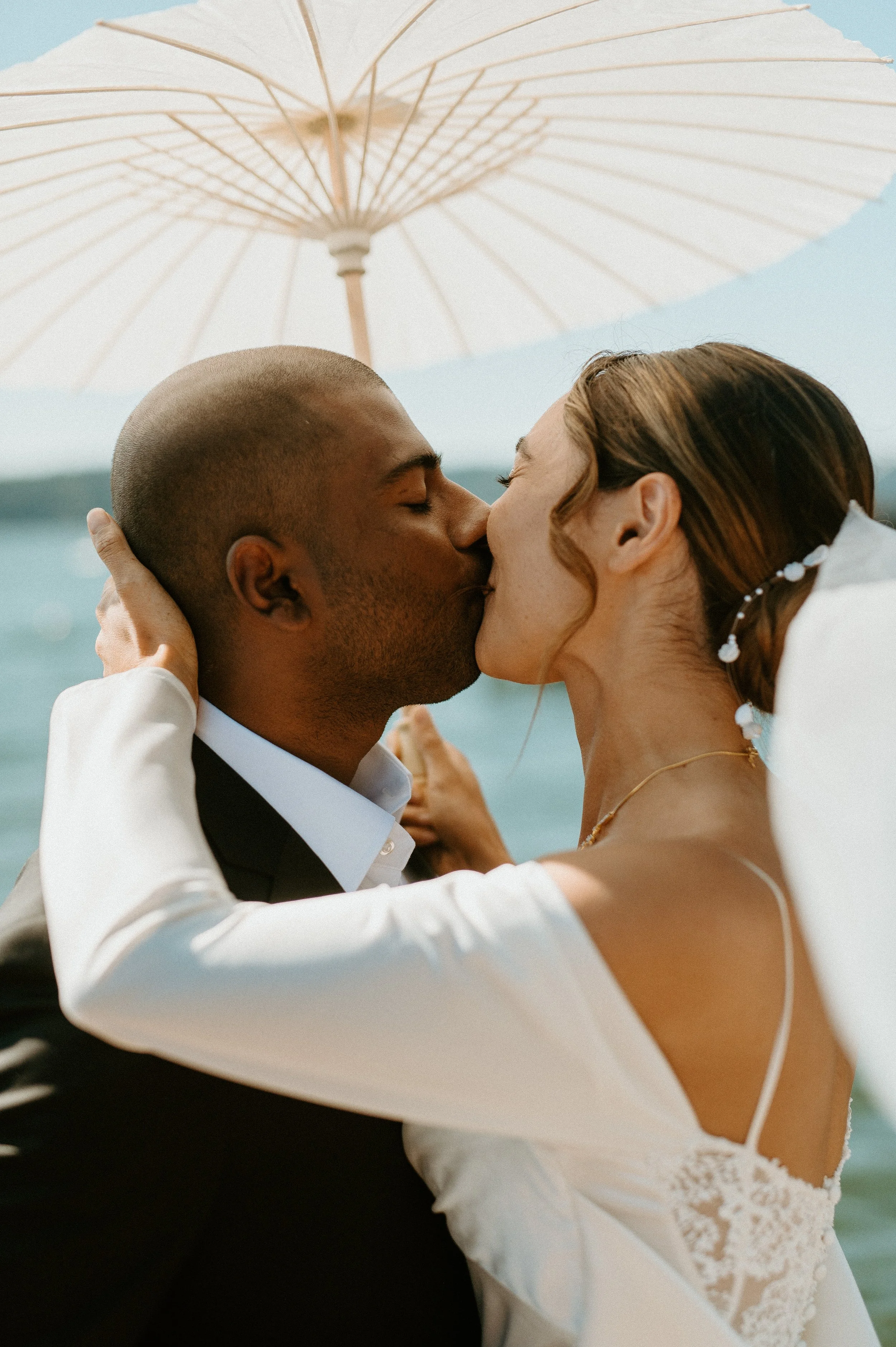Romantic bride and groom kissing by the water under parasol at Seattle backyard wedding
