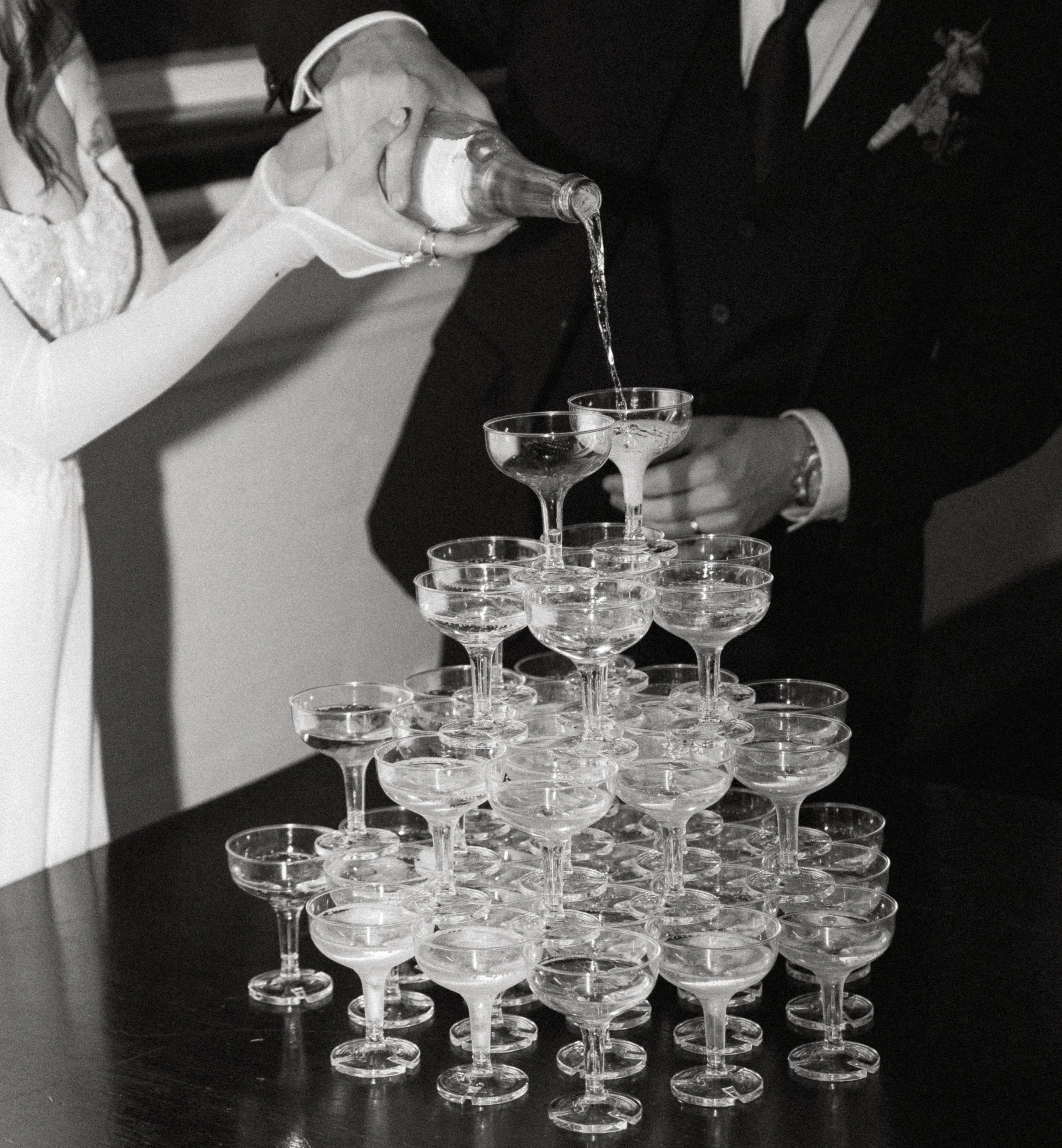 Black and white detail photo of champagne being poured into a champagne tower during an intimate wedding reception