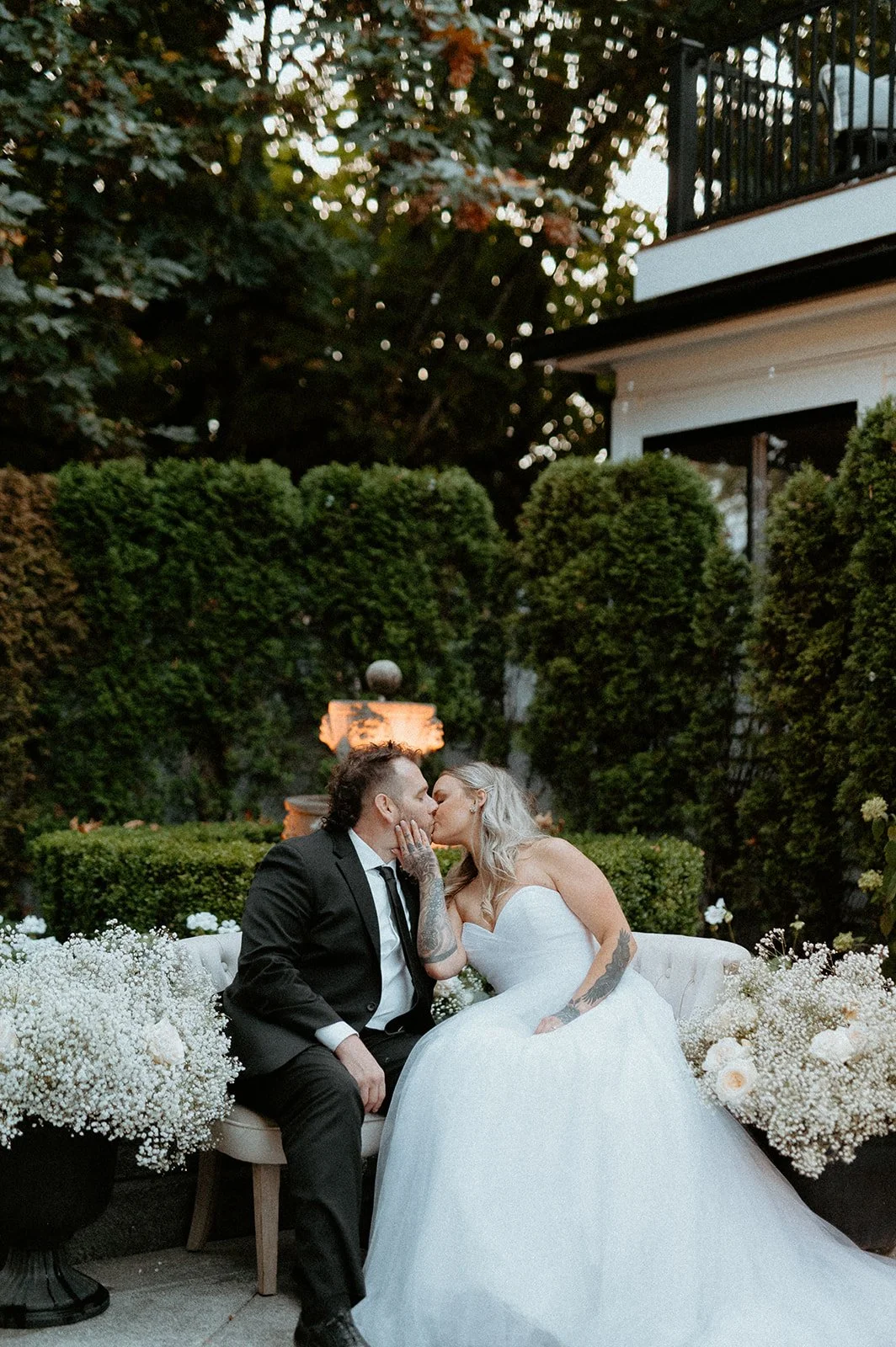 bride + and + groom + kissing + while sitting + on + lounge seating + at + The Orting Manor + in + Orting Washington + during + outdoor wedding