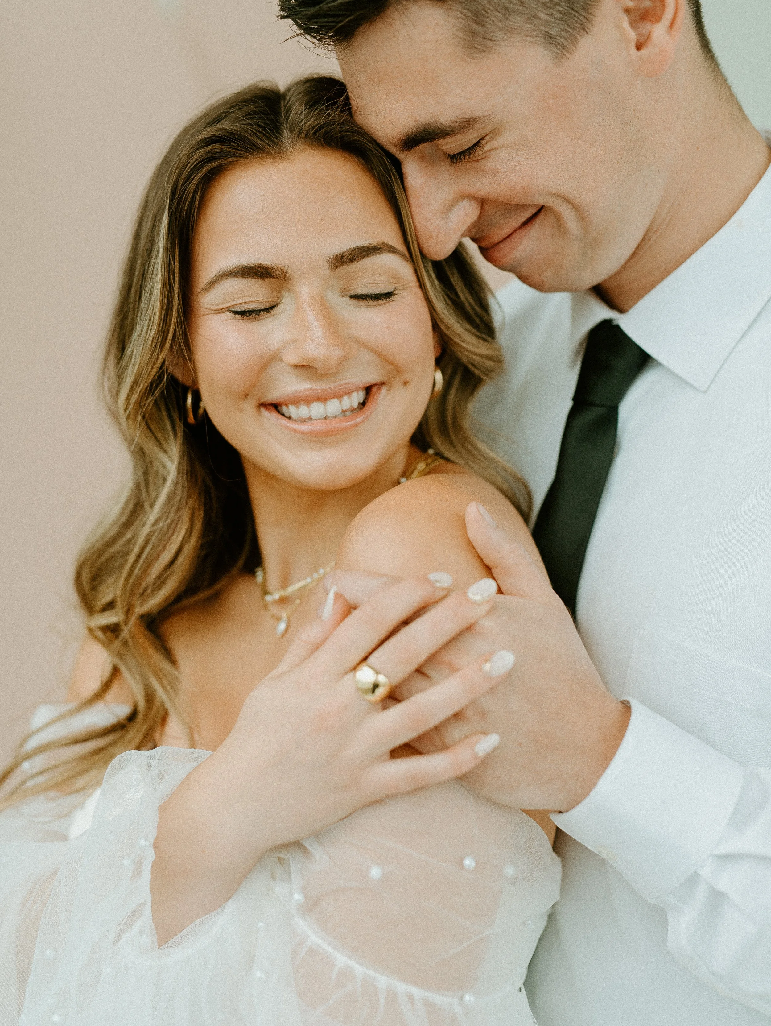 close up of bride smiling with groom embracing her in soft romantic studio portrait