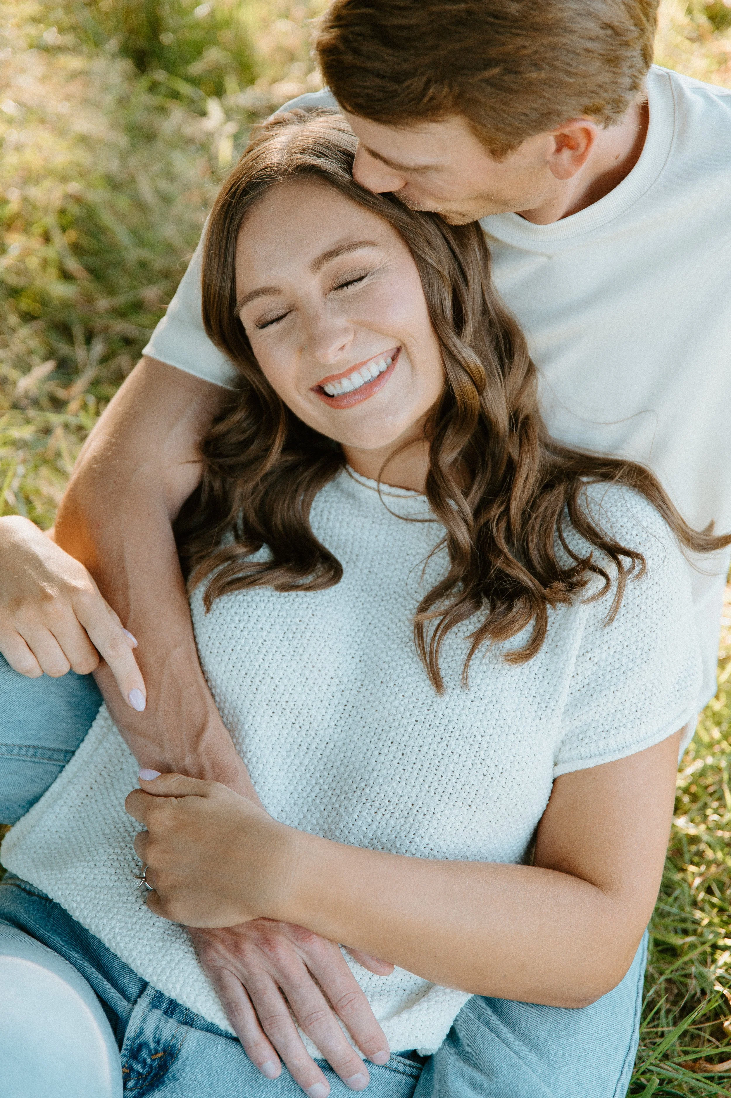 Engaged couple cuddling in a grassy field as he kisses her forehead during their golden hour engagement session in North Bend, Washington