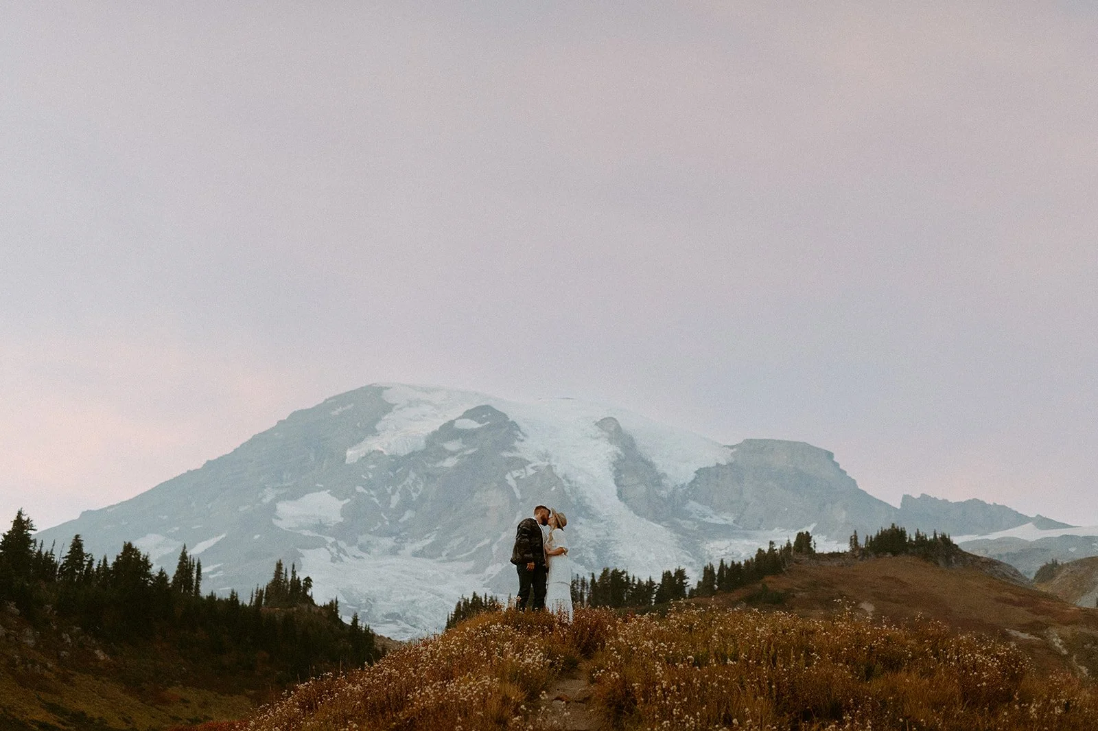 Couple standing on a ridge with Mount Rainier in the background during a misty fall engagement session