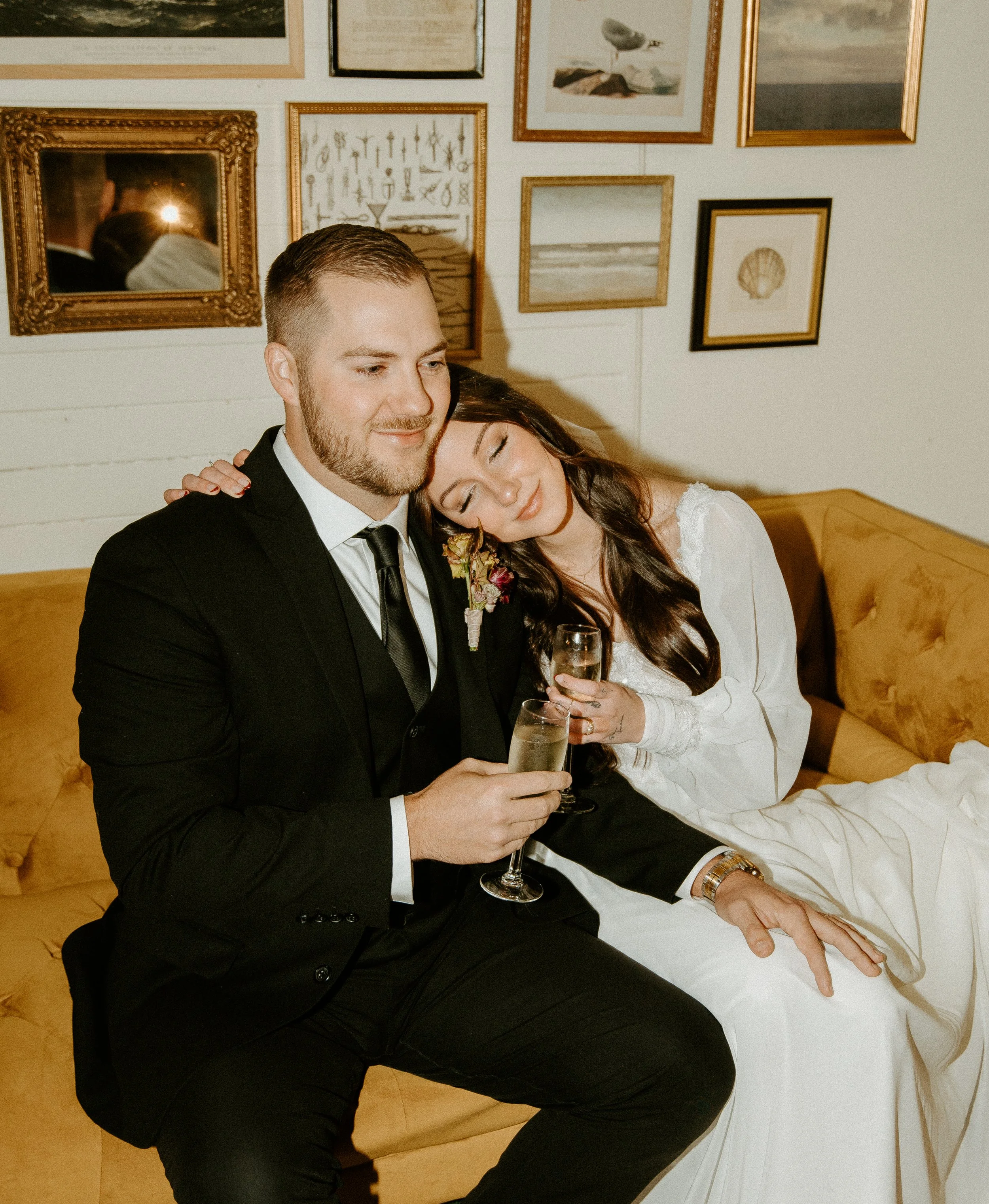Cozy candid portrait of bride and groom relaxing on a mustard velvet couch with champagne glasses during an intimate Seattle wedding reception