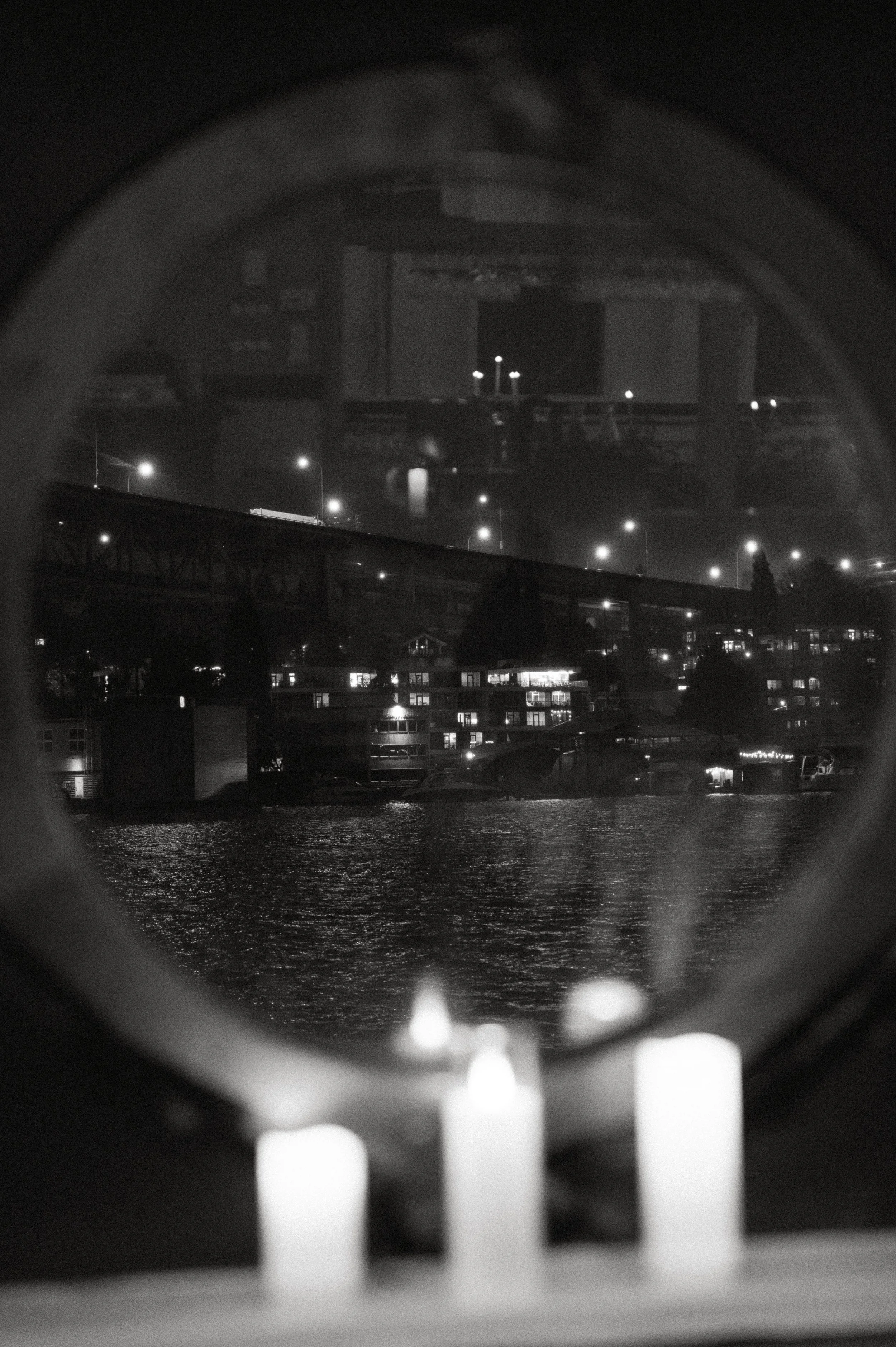 Black and white nighttime view of Seattle waterfront lights reflected through a round boat window during a romantic wedding reception