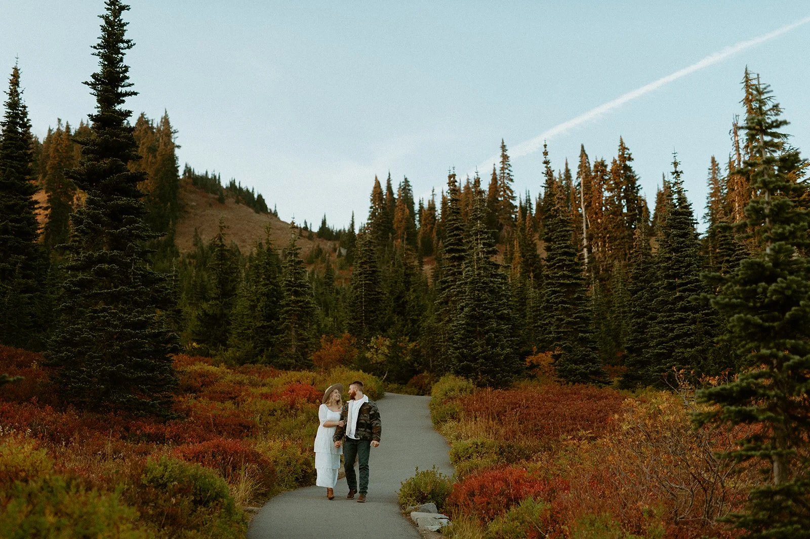 Couple walking along a winding trail surrounded by evergreen trees and fall foliage at Mount Rainier