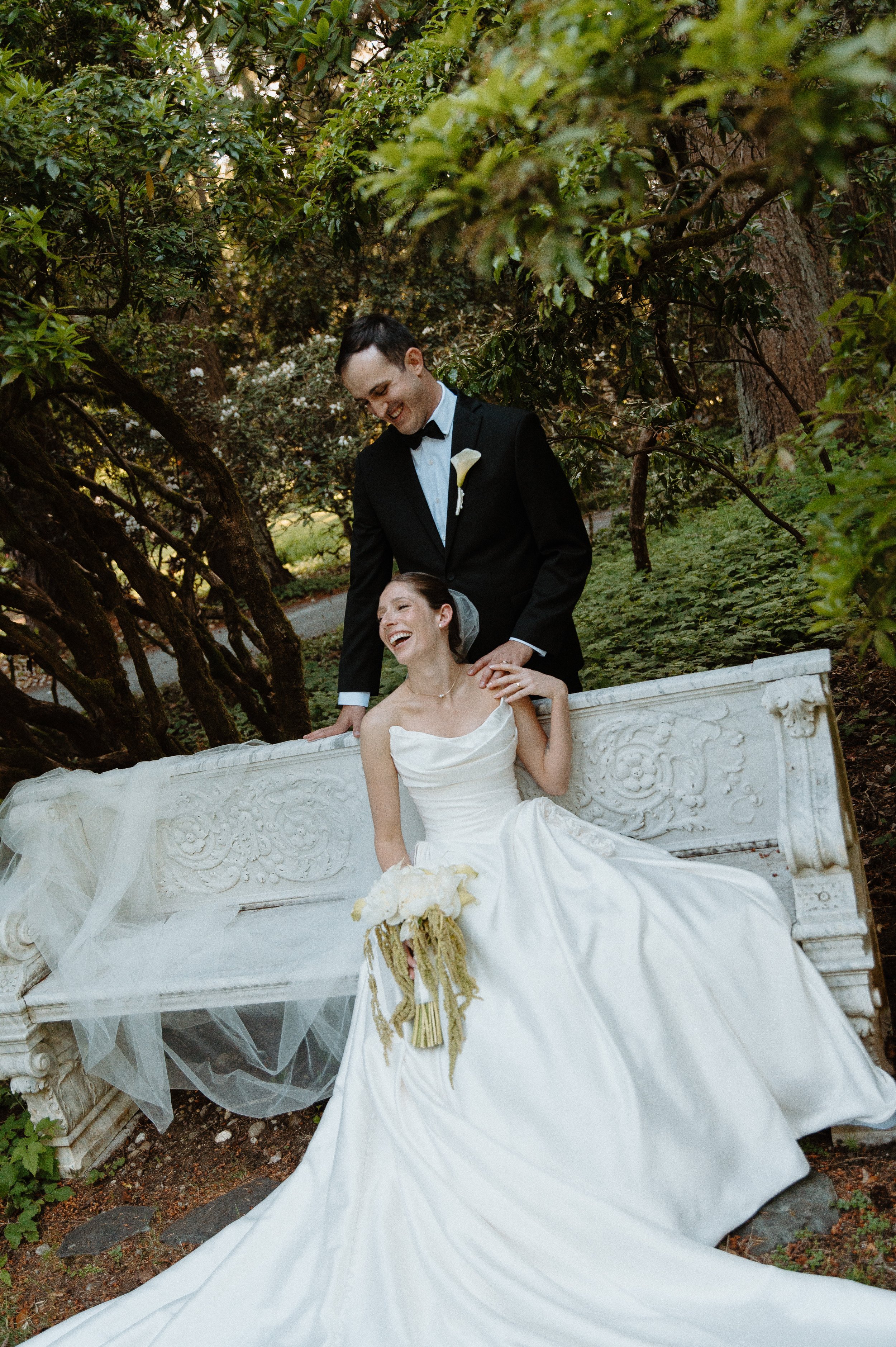 Bride and groom laughing together on a garden bench at Lakewold Gardens in Lakewood, Washington.