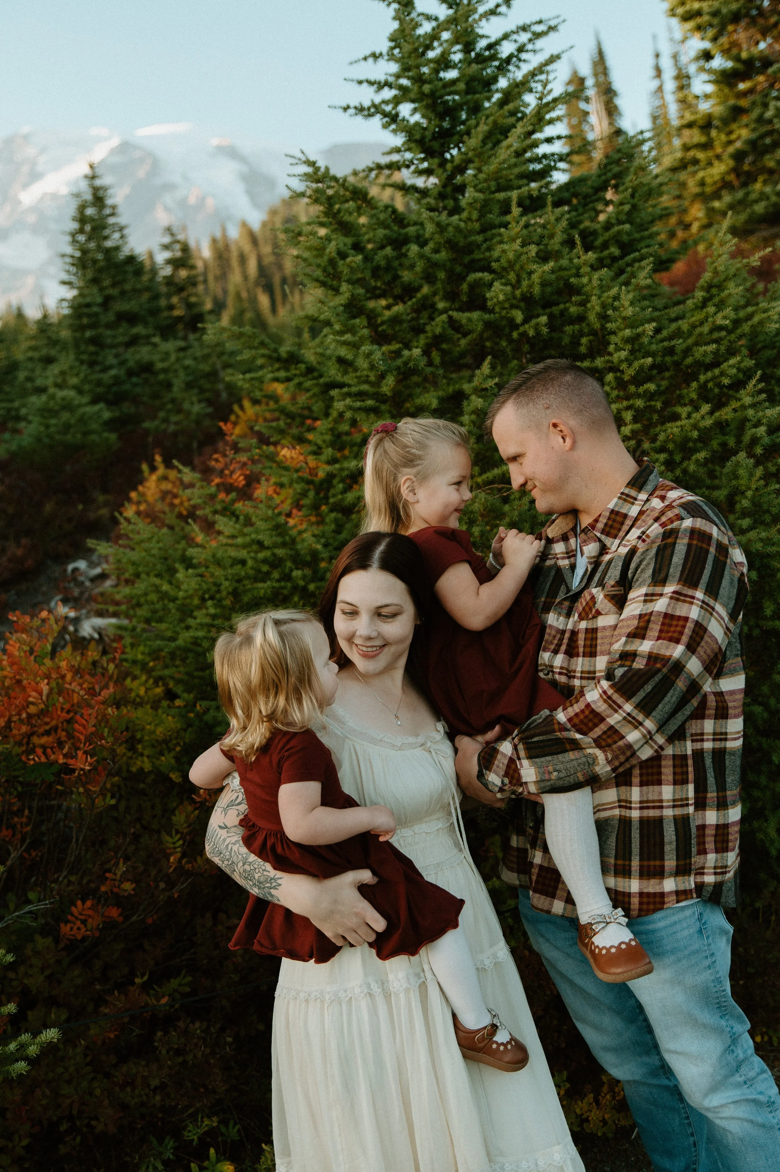     .    Family of four cuddling together among colorful fall foliage and evergreens during a Mount Rainier family session