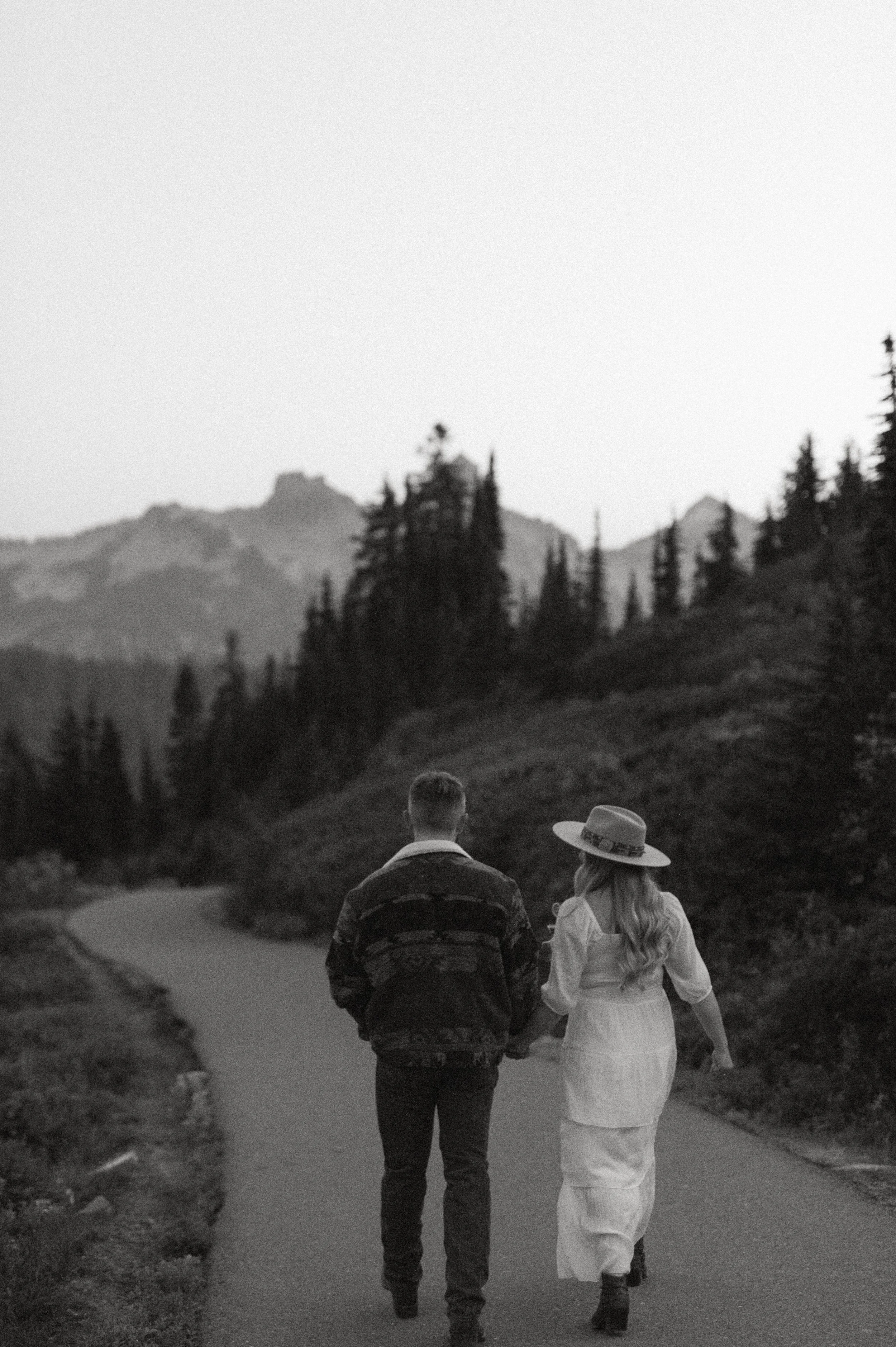 Black and white photo of couple walking hand in hand down a quiet mountain road