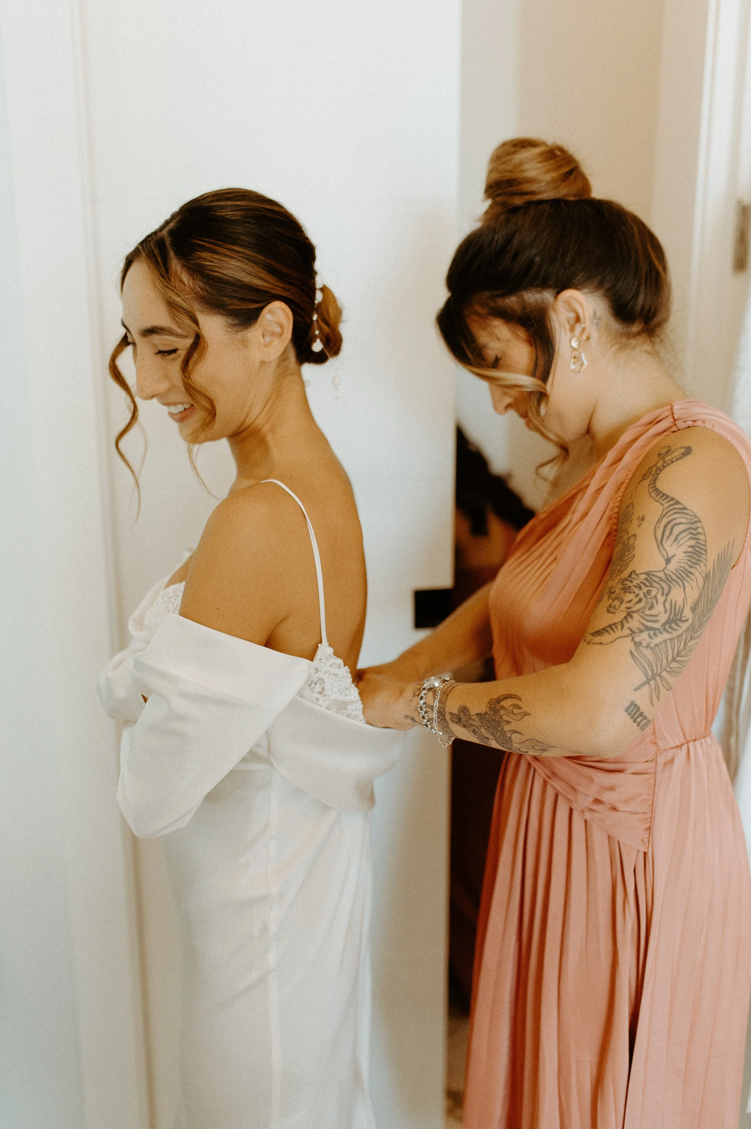 Bridesmaid helping bride into wedding dress during intimate Seattle backyard wedding morning