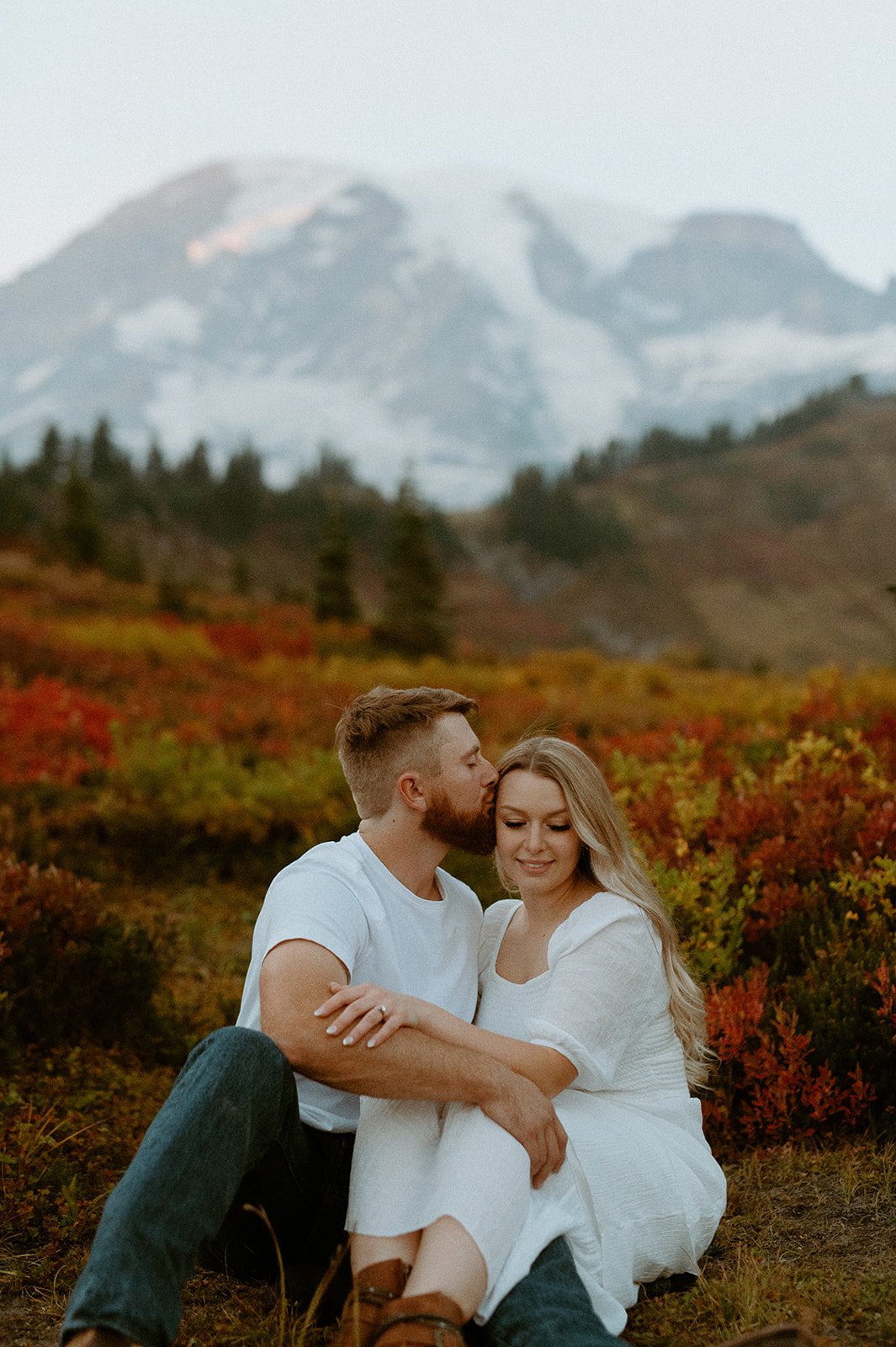 Romantic seated portrait of couple in fall colors with Mount Rainier softly blurred in the background