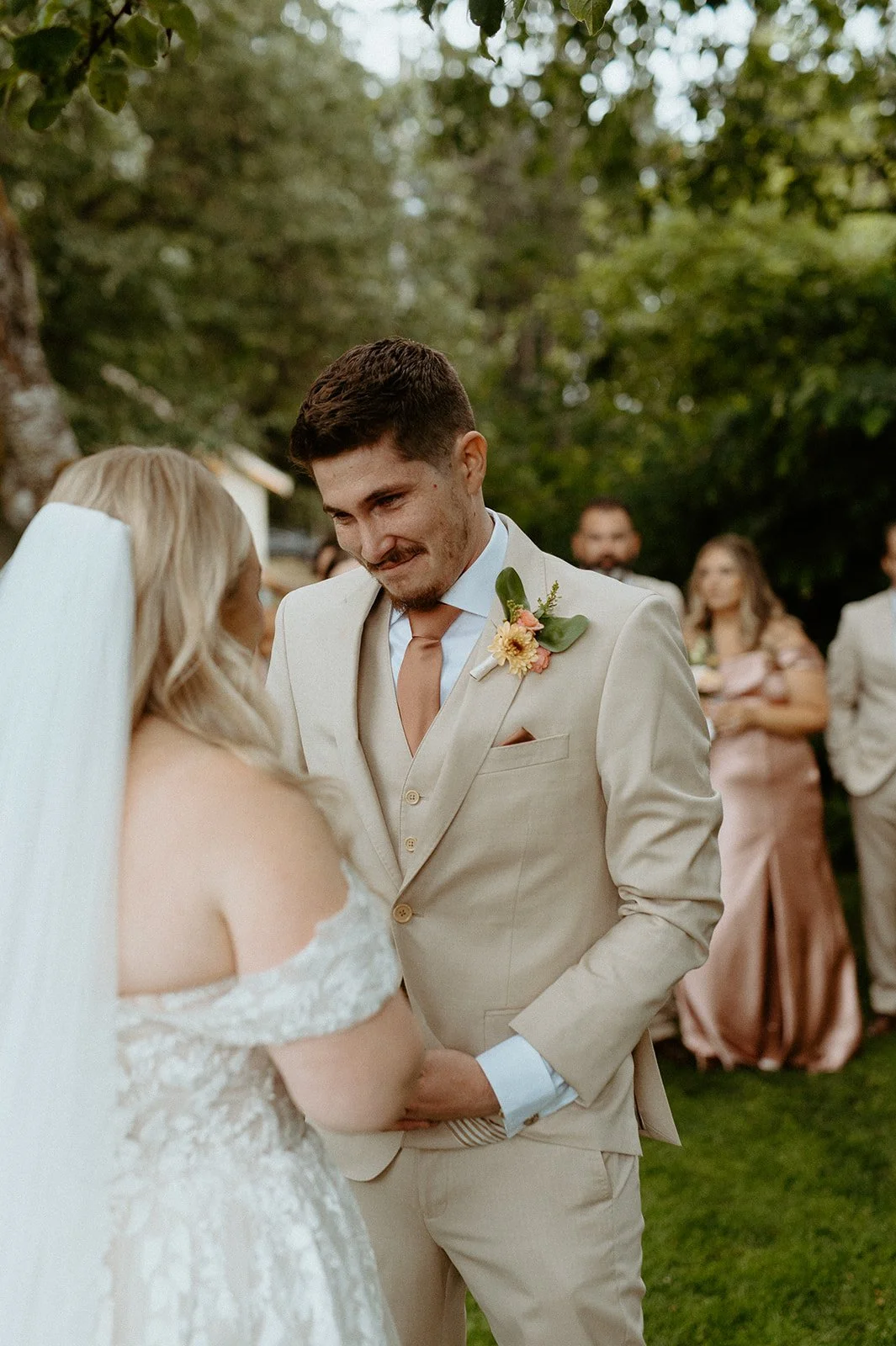 Groom reacting emotionally during wedding ceremony while holding bride’s hands outdoors