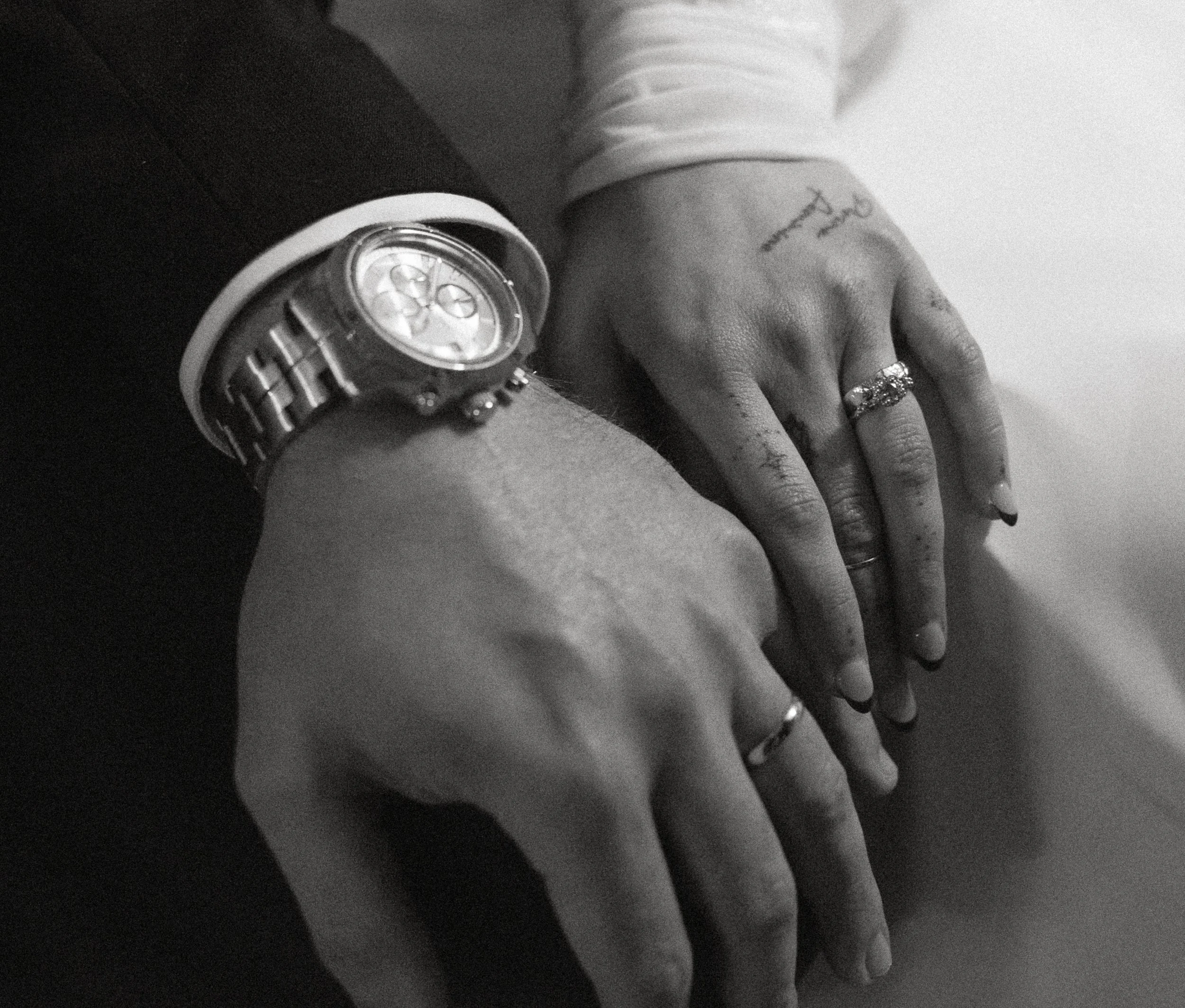 Black and white close up of bride and groom’s hands showing wedding rings and watch detail during their wedding reception