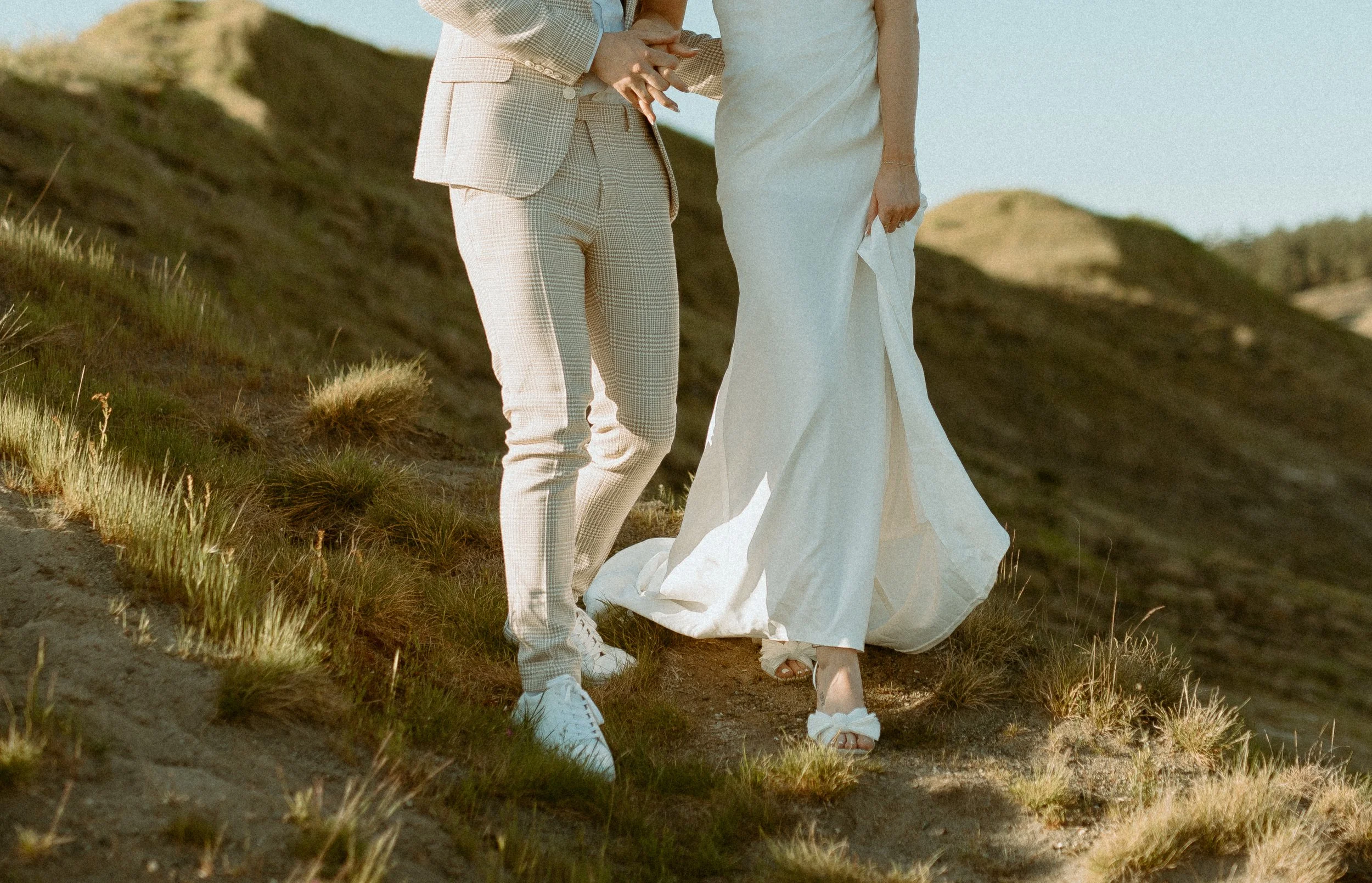 detail photo of couple walking together on grassy hill at Chambers Bay wearing bridal attire