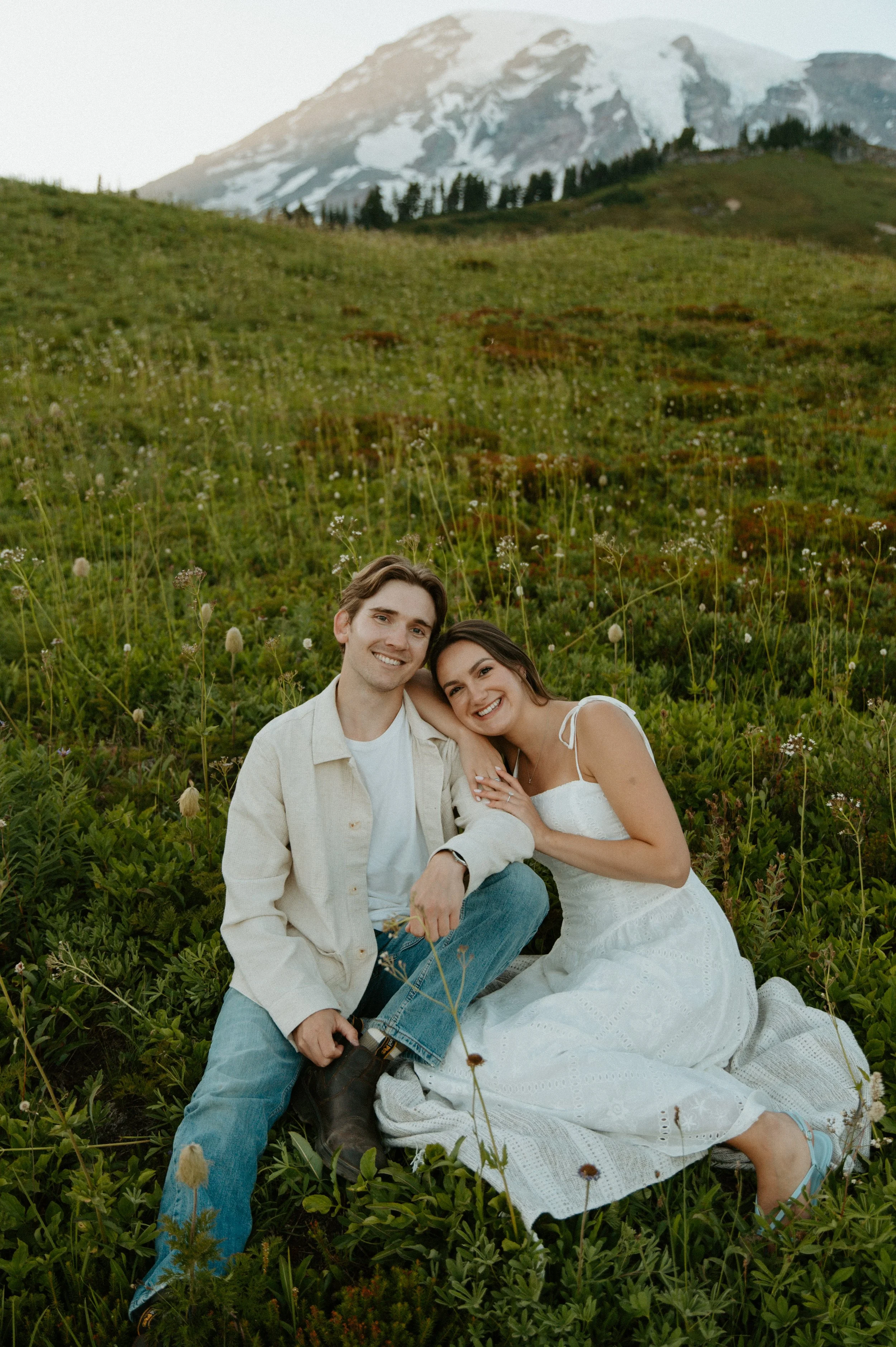 Couple sitting together in a field of wildflowers with Mount Rainier rising behind them.
