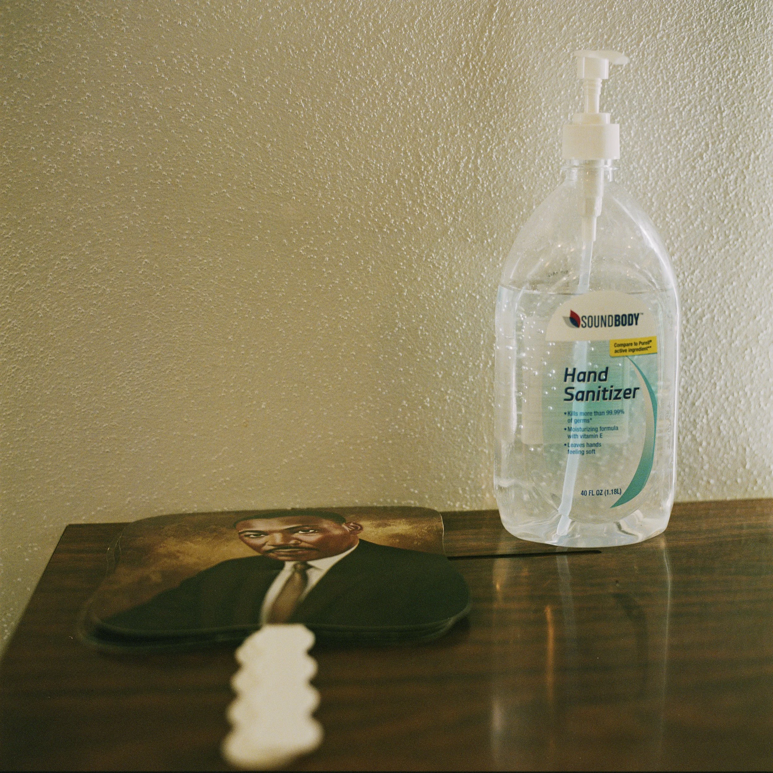 A bottle of hand sanitizer and a mouse pad with a picture of a man in a suit on a wooden surface against a beige wall.