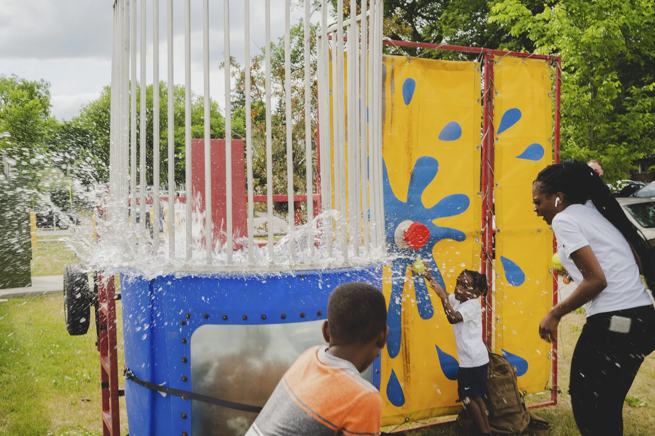 Children and adults enjoying a water crawl activity at an outdoor event, with water splashing and a colorful structure with a yellow and red design.