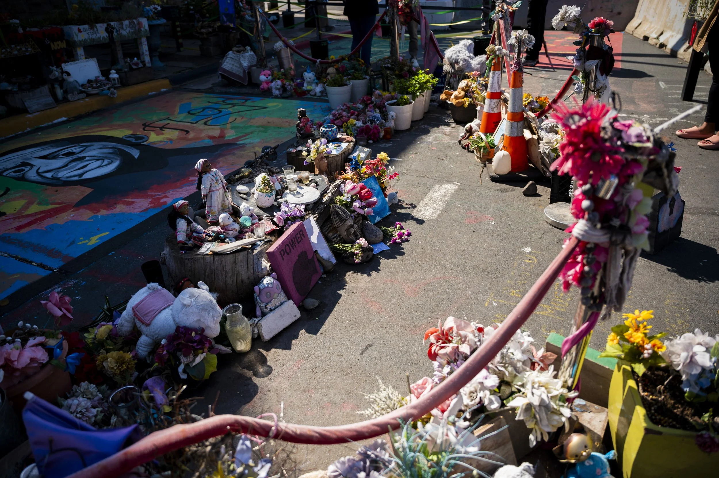 Memorial at a street memorial with flowers, stuffed animals, candles, and framed photographs, reflecting a tribute for a recent tragedy