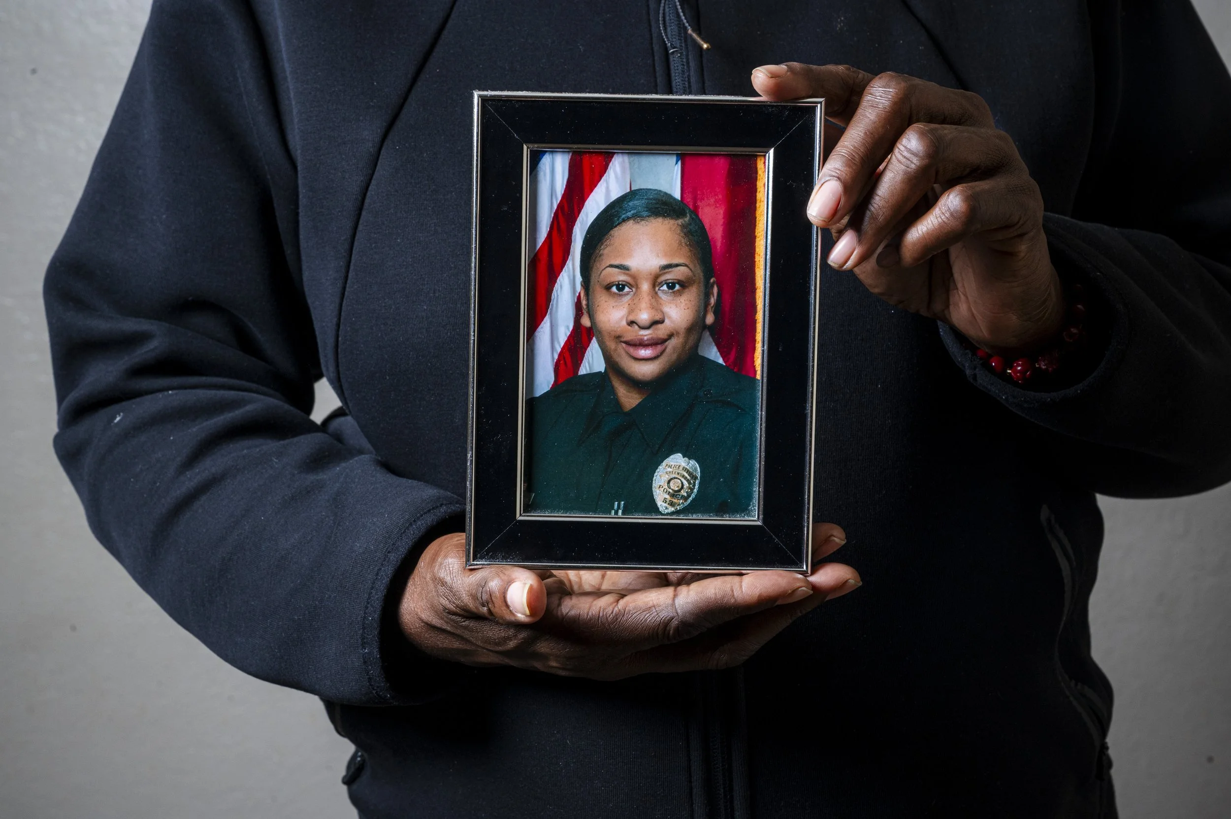 A person holding a framed police officer's portrait with an American flag in the background.