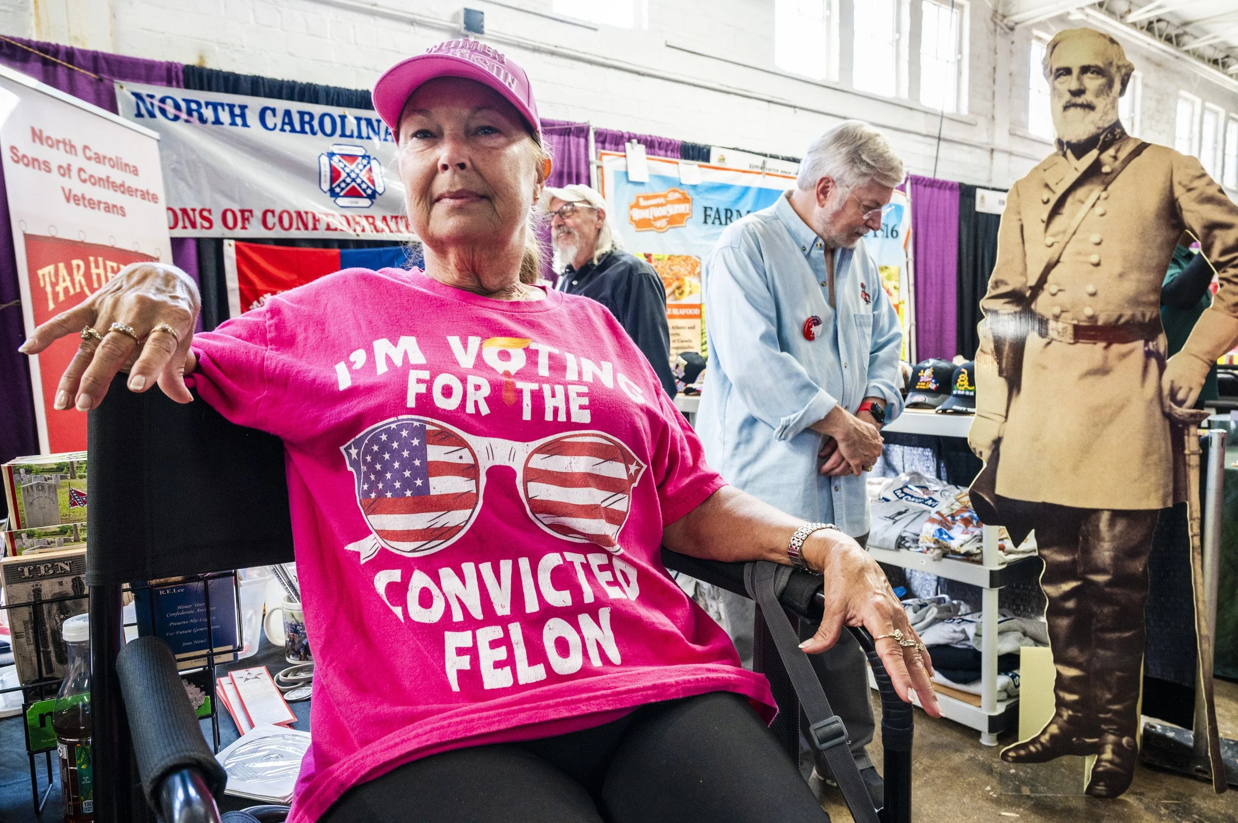 NPR Faye New sports her "I'm voting for the convicted felon" t-shirt and "Women for Mark Robinson" hat in front of the North Carolina Sons of Confederate Veterans booth at the NC State Fair. 2024