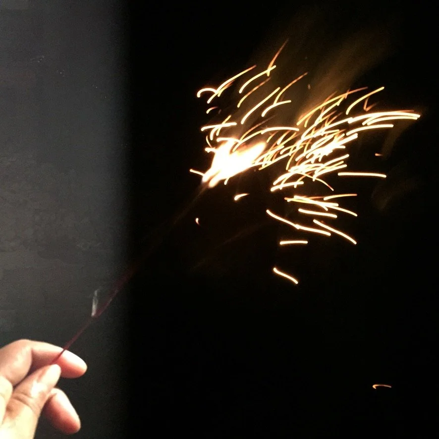 Person holding a lit sparkler against a dark background.