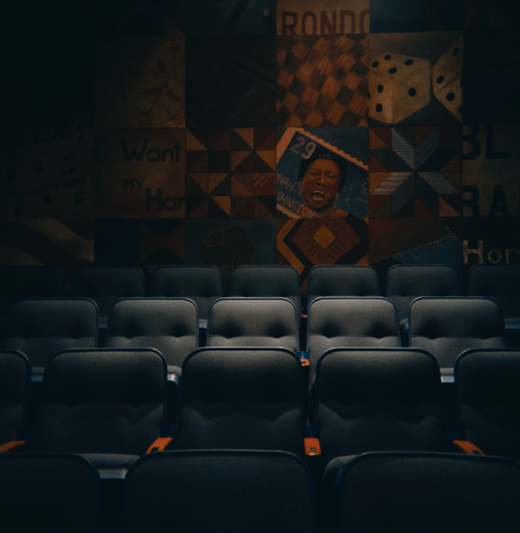 Empty theater seating with a colorful mural on the wall featuring a woman's singing face and various patterns.