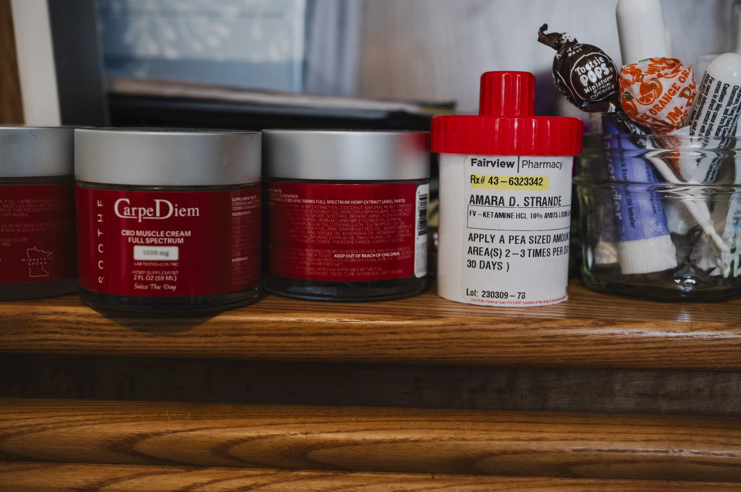 Close-up of a wooden shelf with red-labeled jars, a white bottle with a red cap, and a glass jar with candies and chocolate.