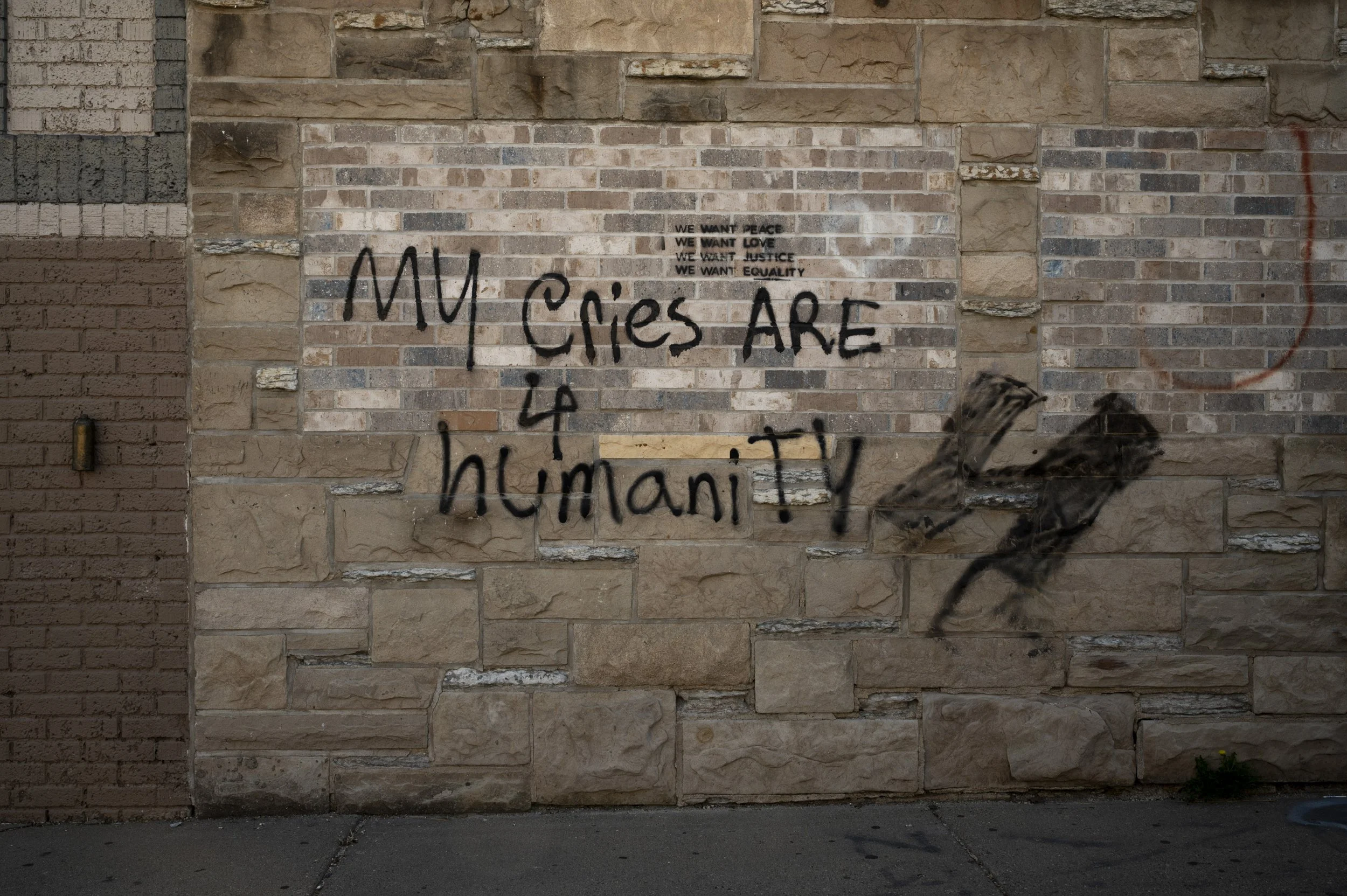Graffiti on a brick wall with the words 'My eyes are 4 humanity' written in black spray paint, and a smaller text above stating 'We want peace, we want love, we want justice, we want equality.'