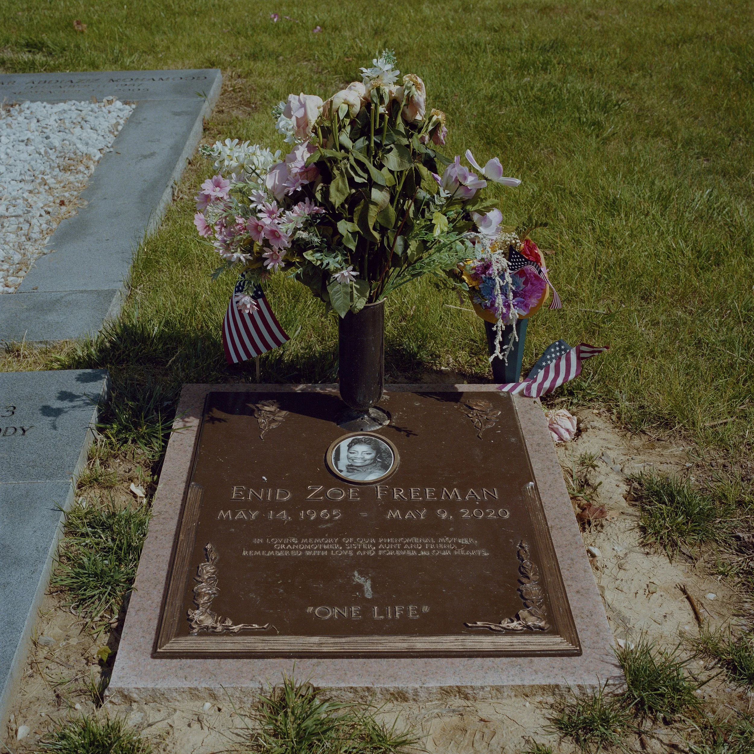 Gravestone of Enid Zoe Freeman with a portrait photo, flowers, and American flags around it.