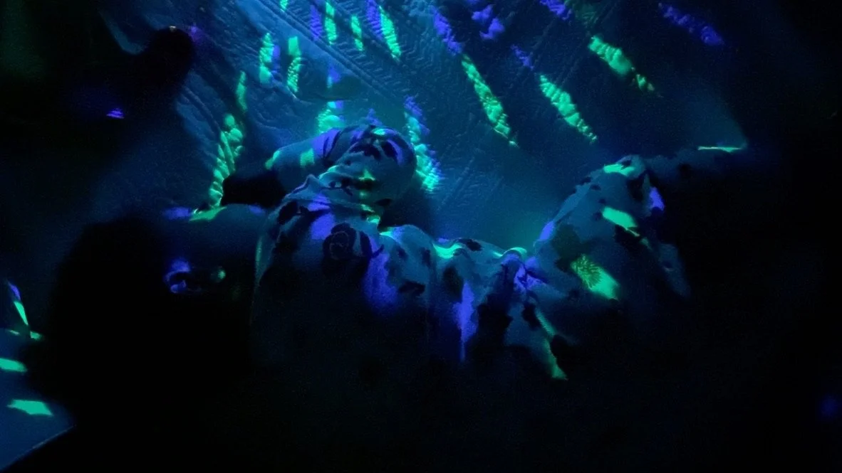Child lying on a blanket in a dark room with glow-in-the-dark patterns projected onto the ceiling and their clothing.