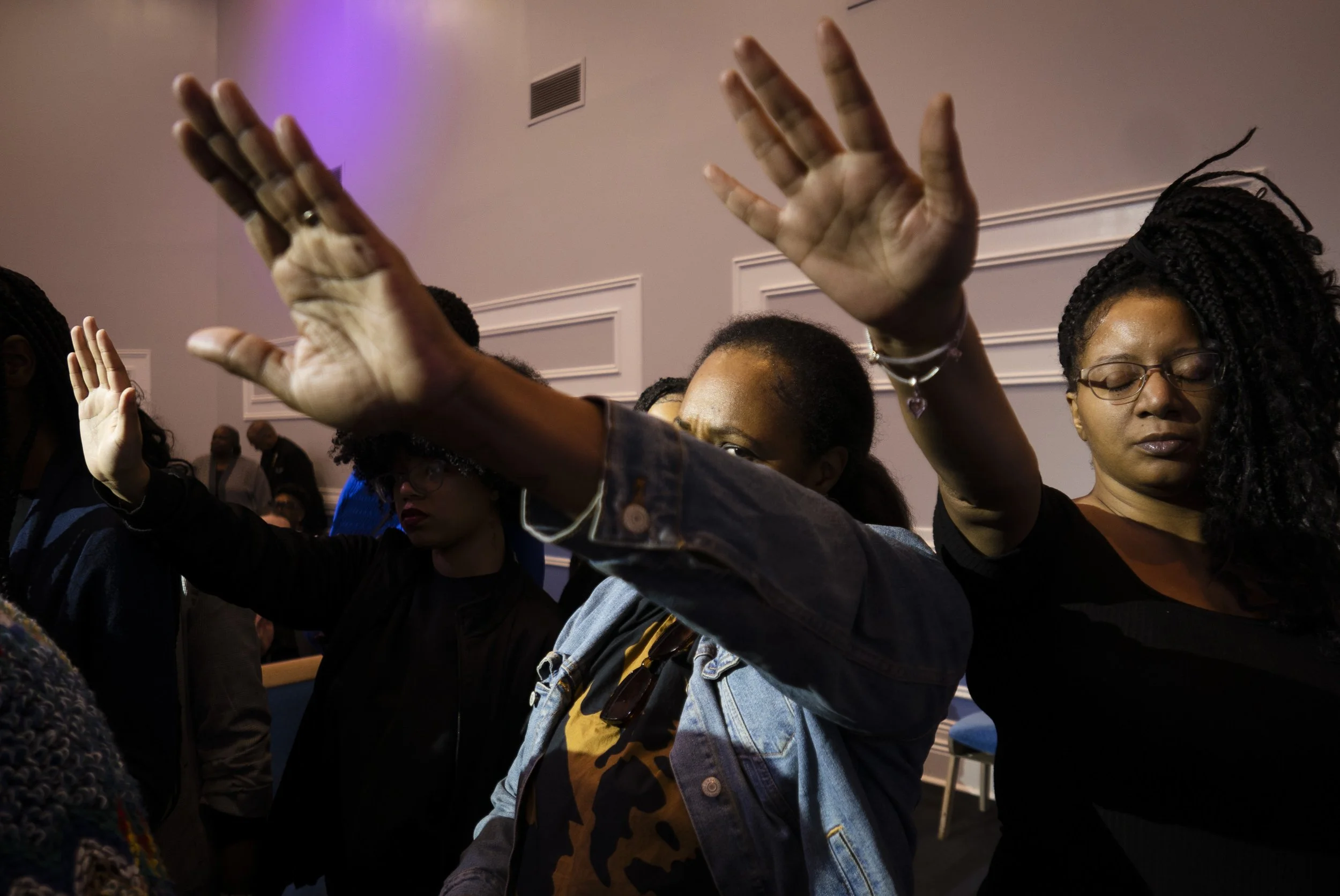 Group of people with eyes closed and hands raised in prayer or worship at a religious gathering.