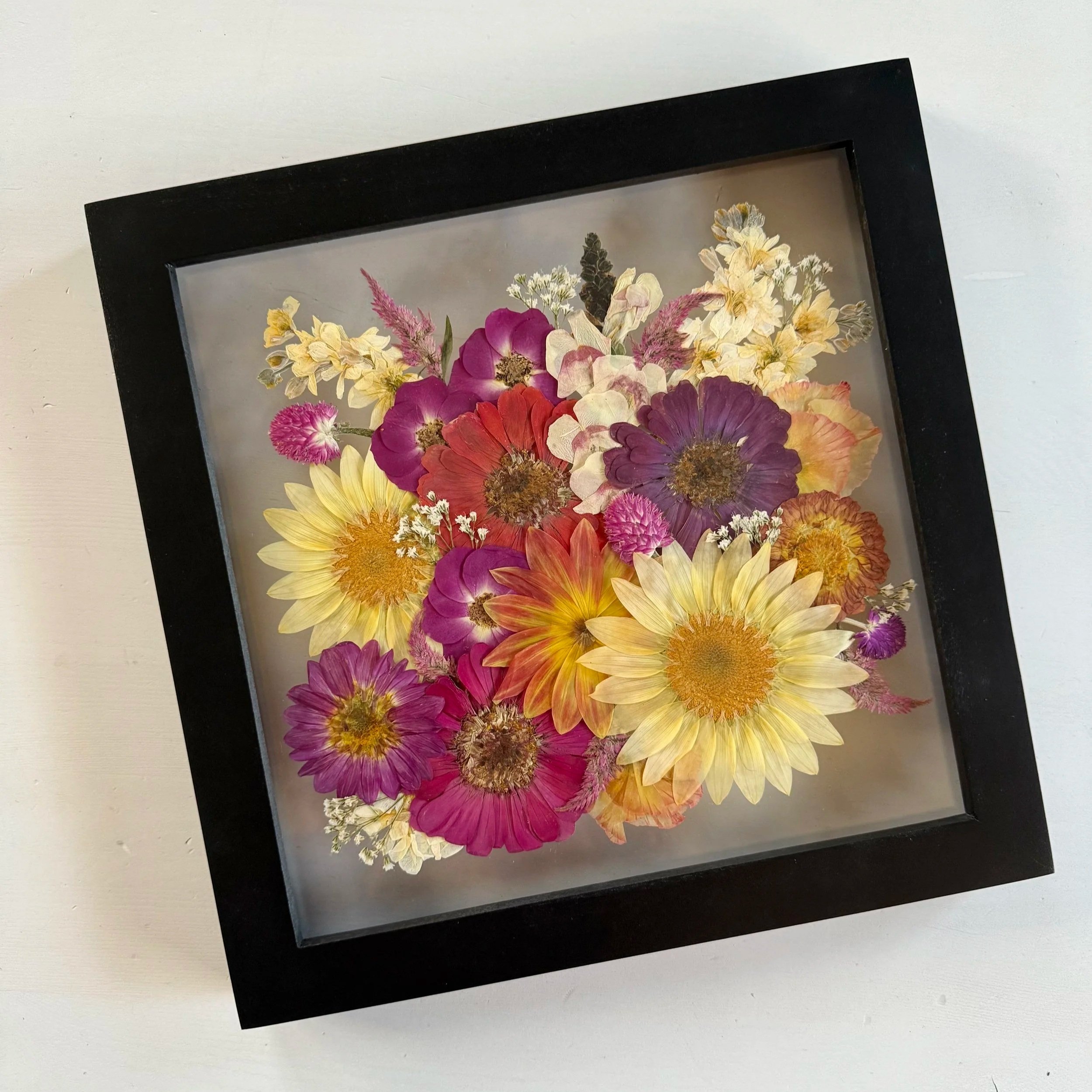 Framed pressed wedding bouquet flowers preserved in a floating glass frame.