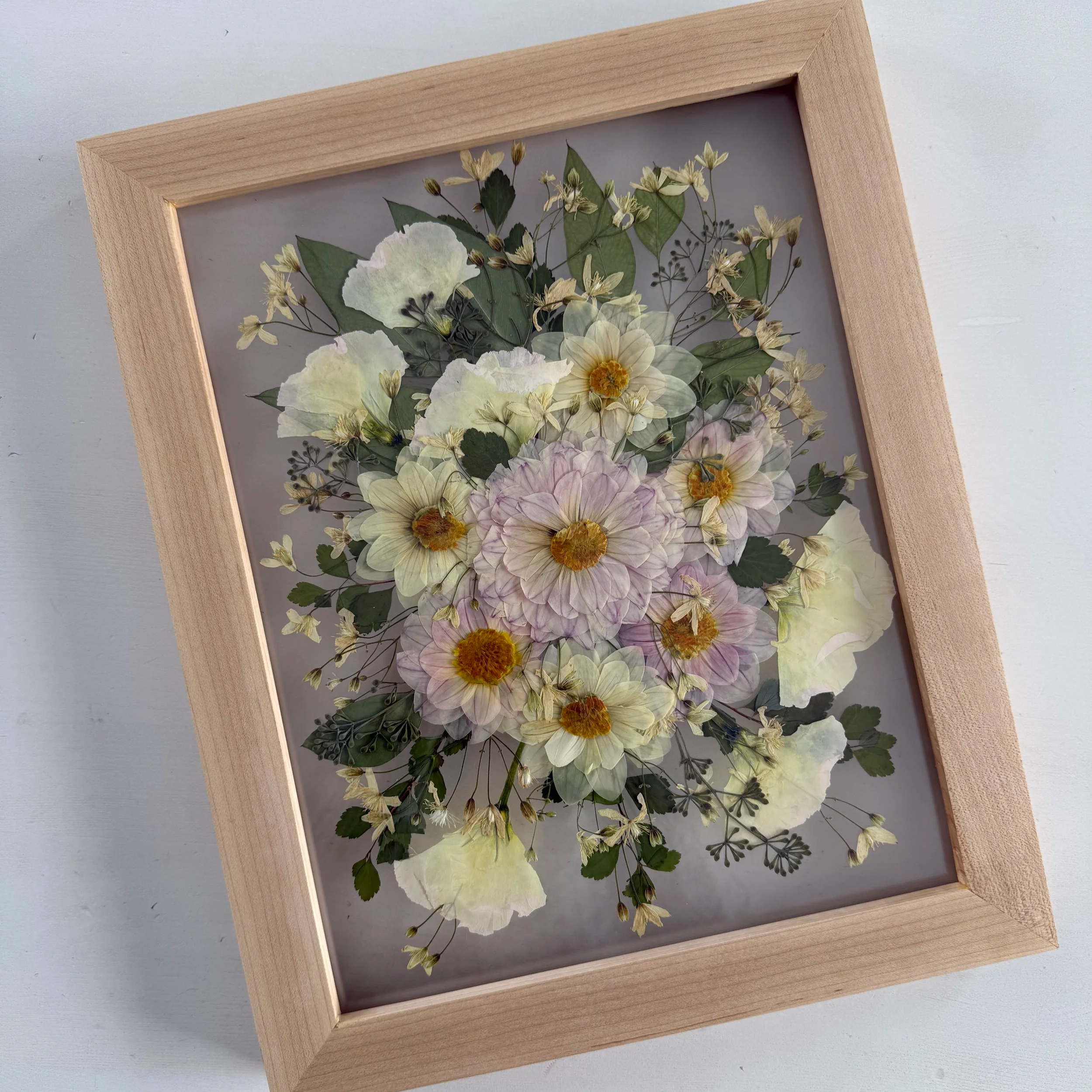 Framed pressed wedding bouquet flowers preserved in a floating glass frame.