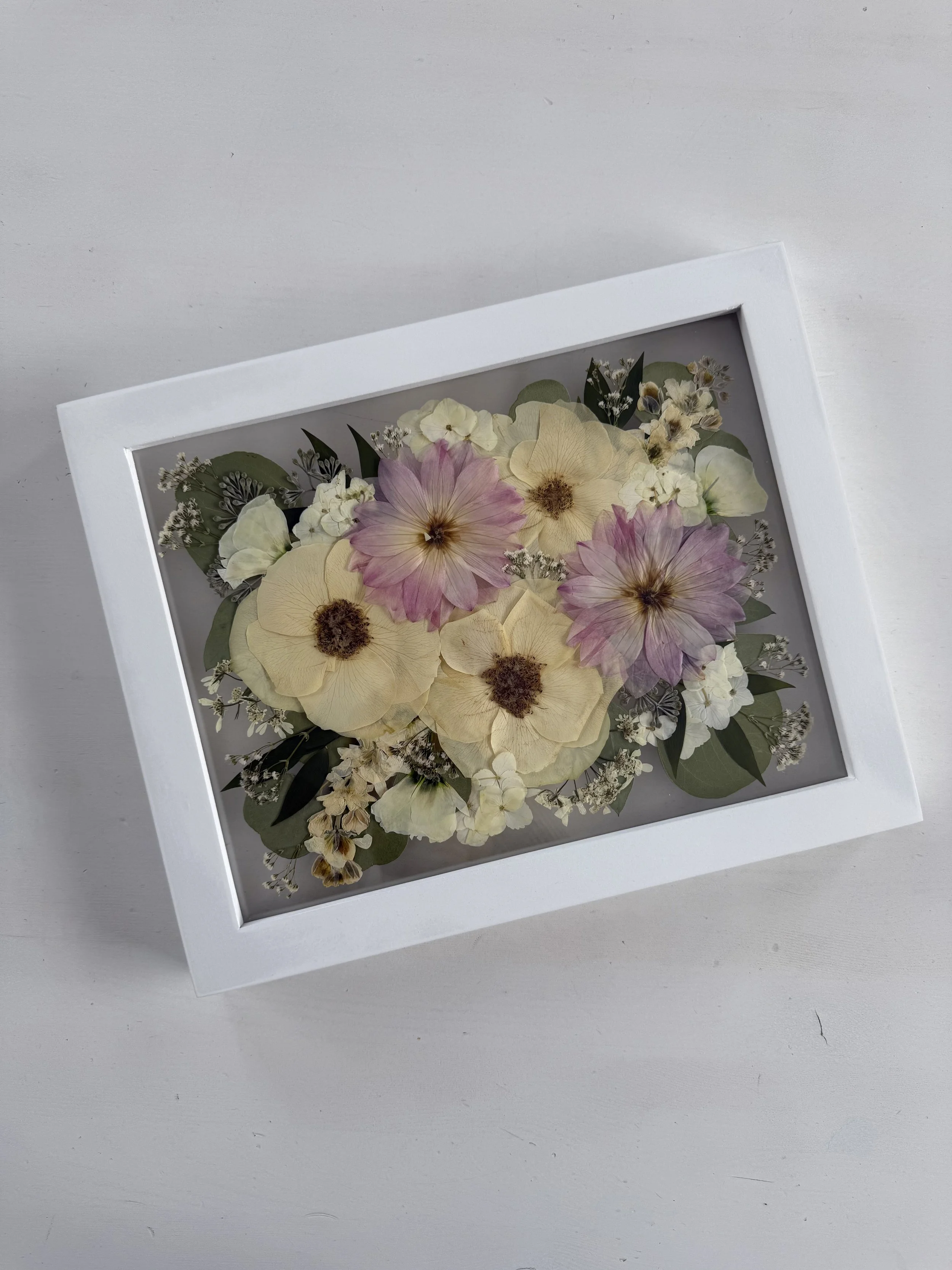 Framed pressed wedding bouquet flowers preserved in a floating glass frame.