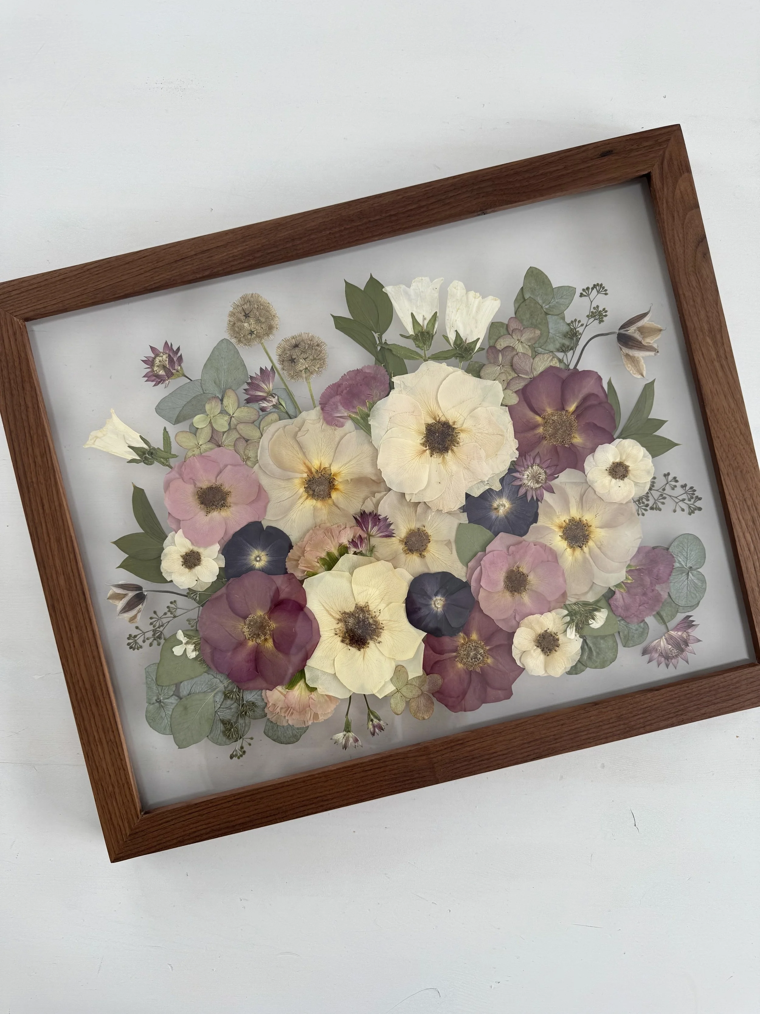 Framed pressed wedding bouquet flowers preserved in a floating glass frame.