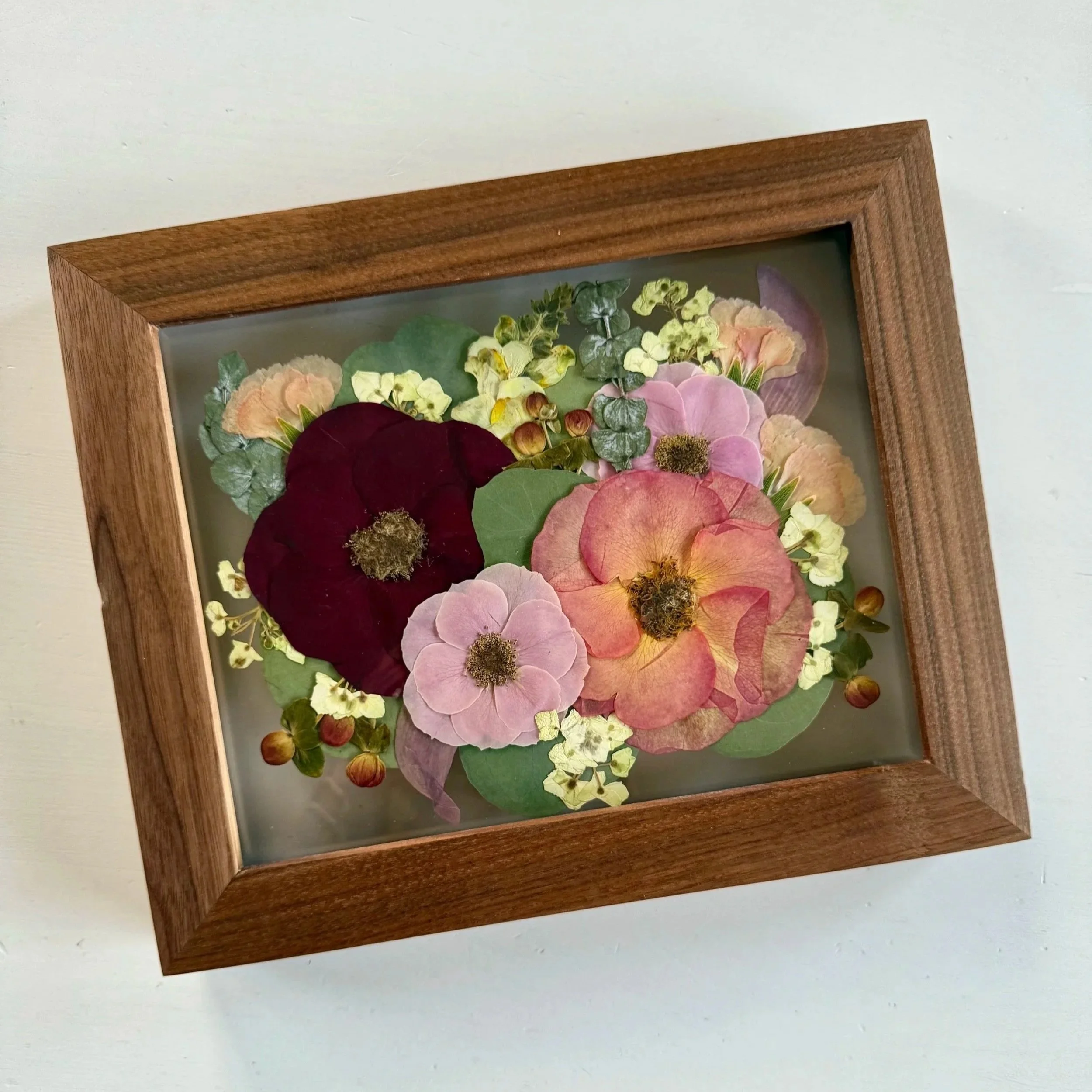 Framed pressed wedding bouquet flowers preserved in a floating glass frame.
