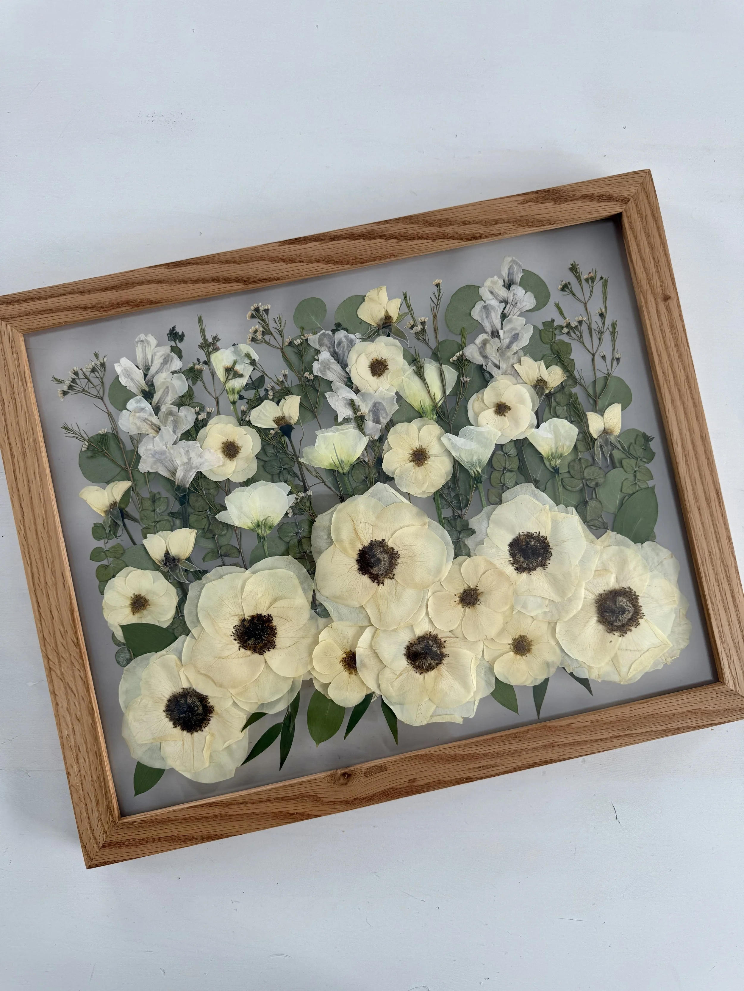 Framed pressed wedding bouquet flowers preserved in a floating glass frame.