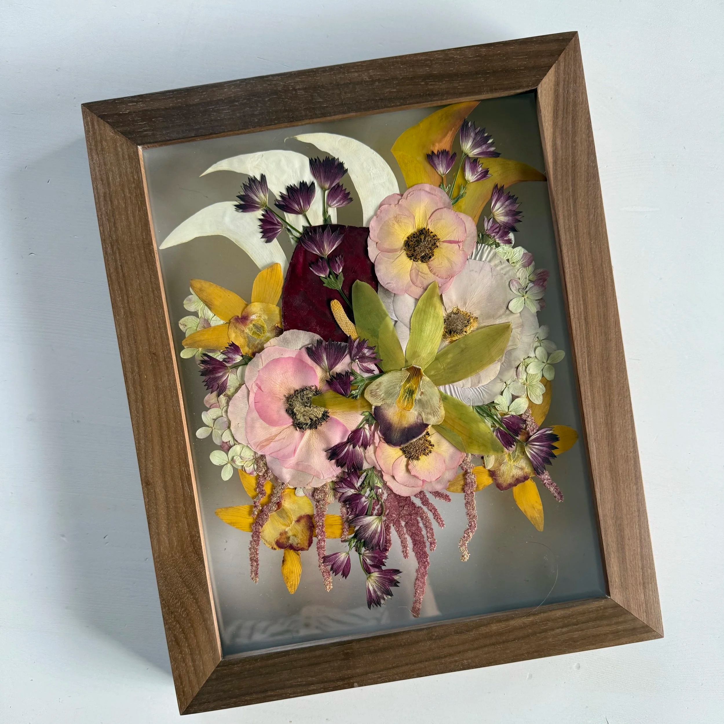 Framed pressed wedding bouquet flowers preserved in a floating glass frame.