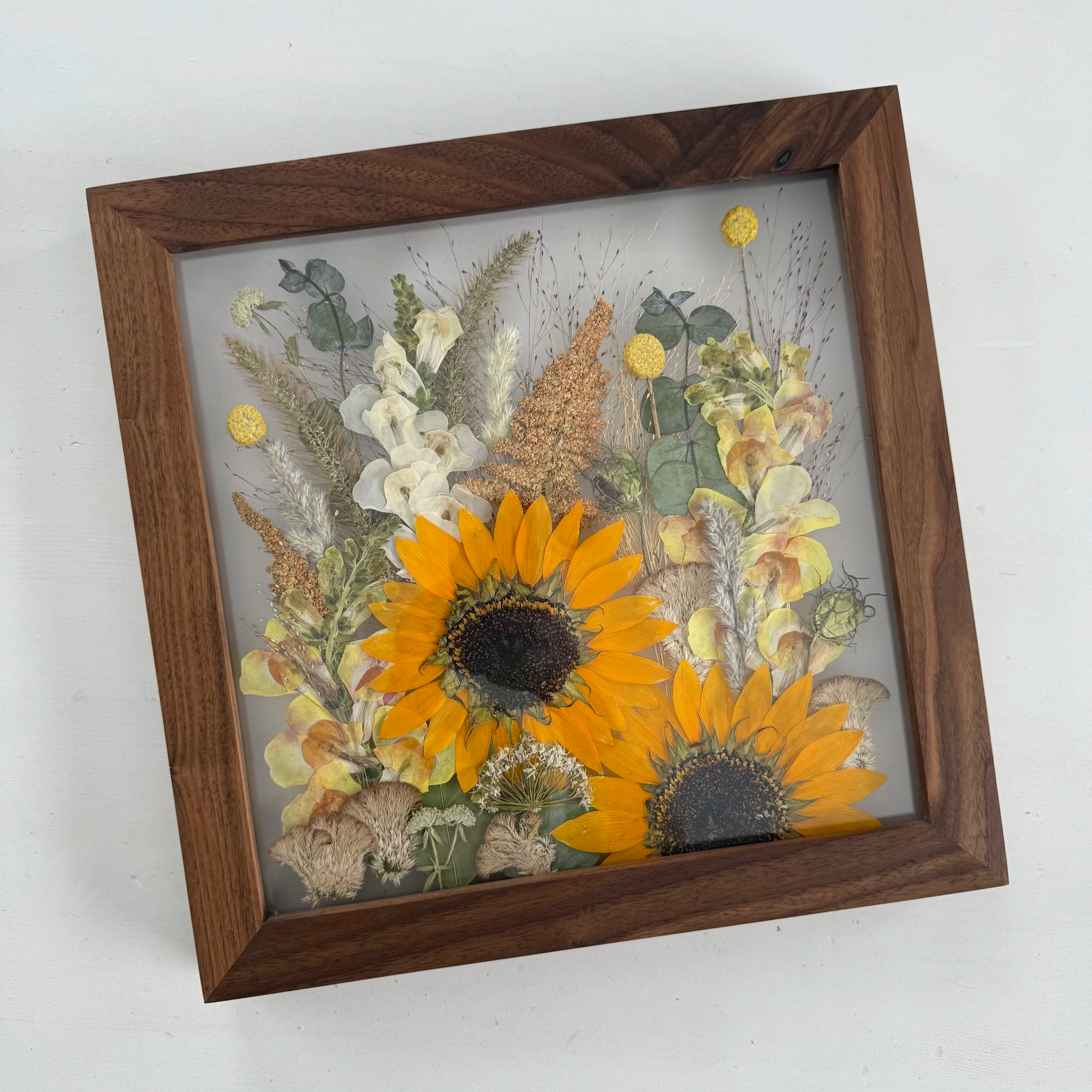Framed pressed wedding bouquet flowers preserved in a floating glass frame.